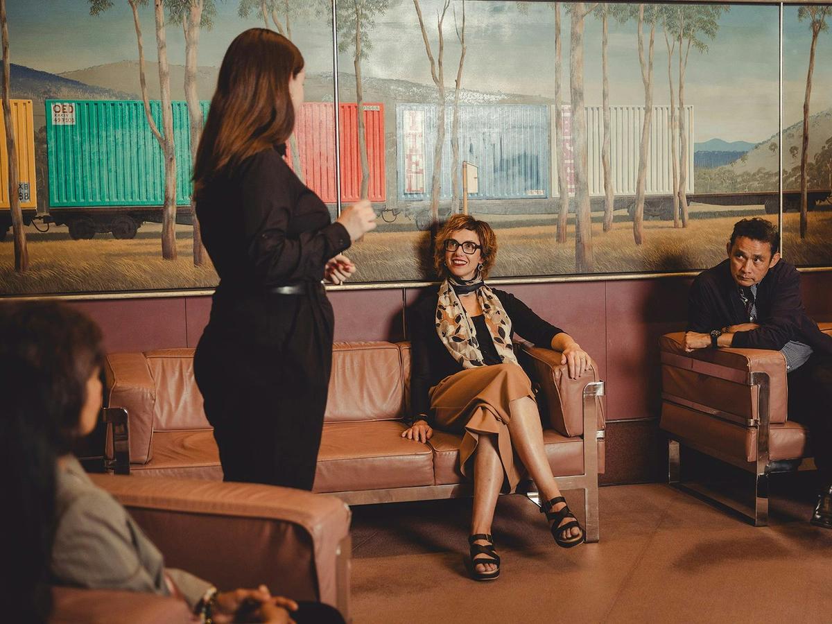 Tour guide talking with two people actively listening, back of a third person blurred in the corner.