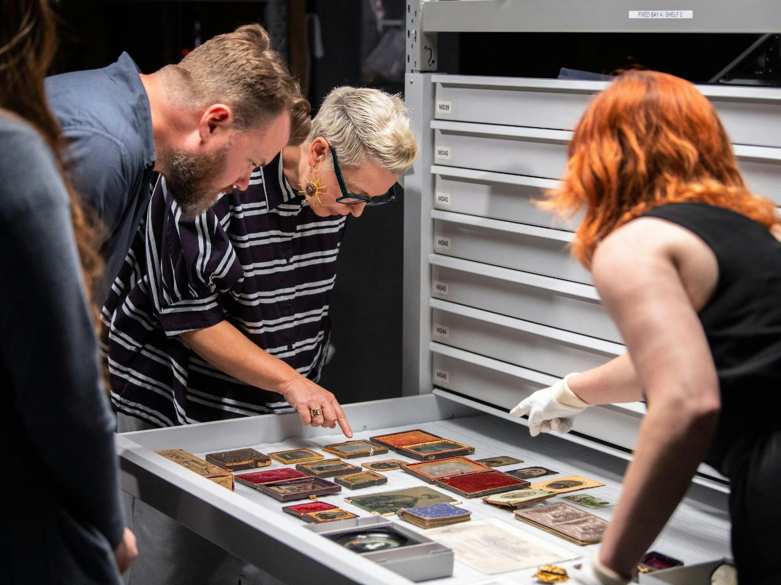Two women and man looking at historical portraits in pulled-out drawer
