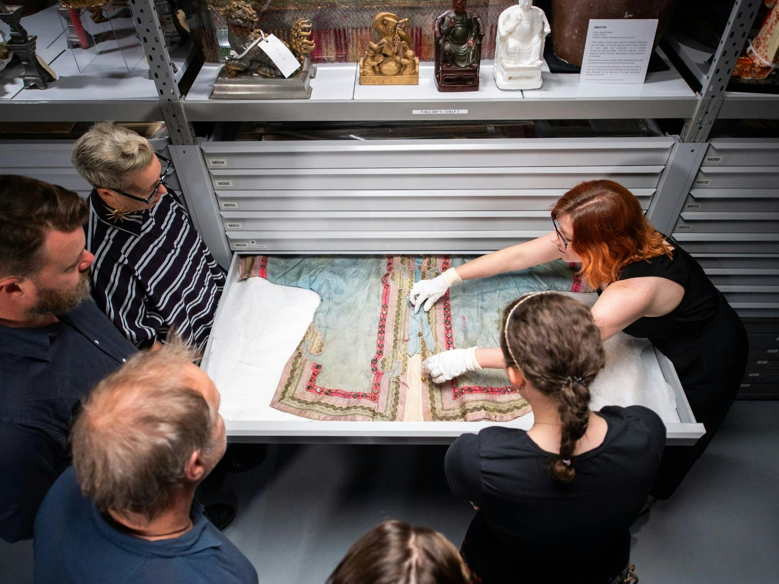 Curator showing historical Chinese jacket in drawer to tour group