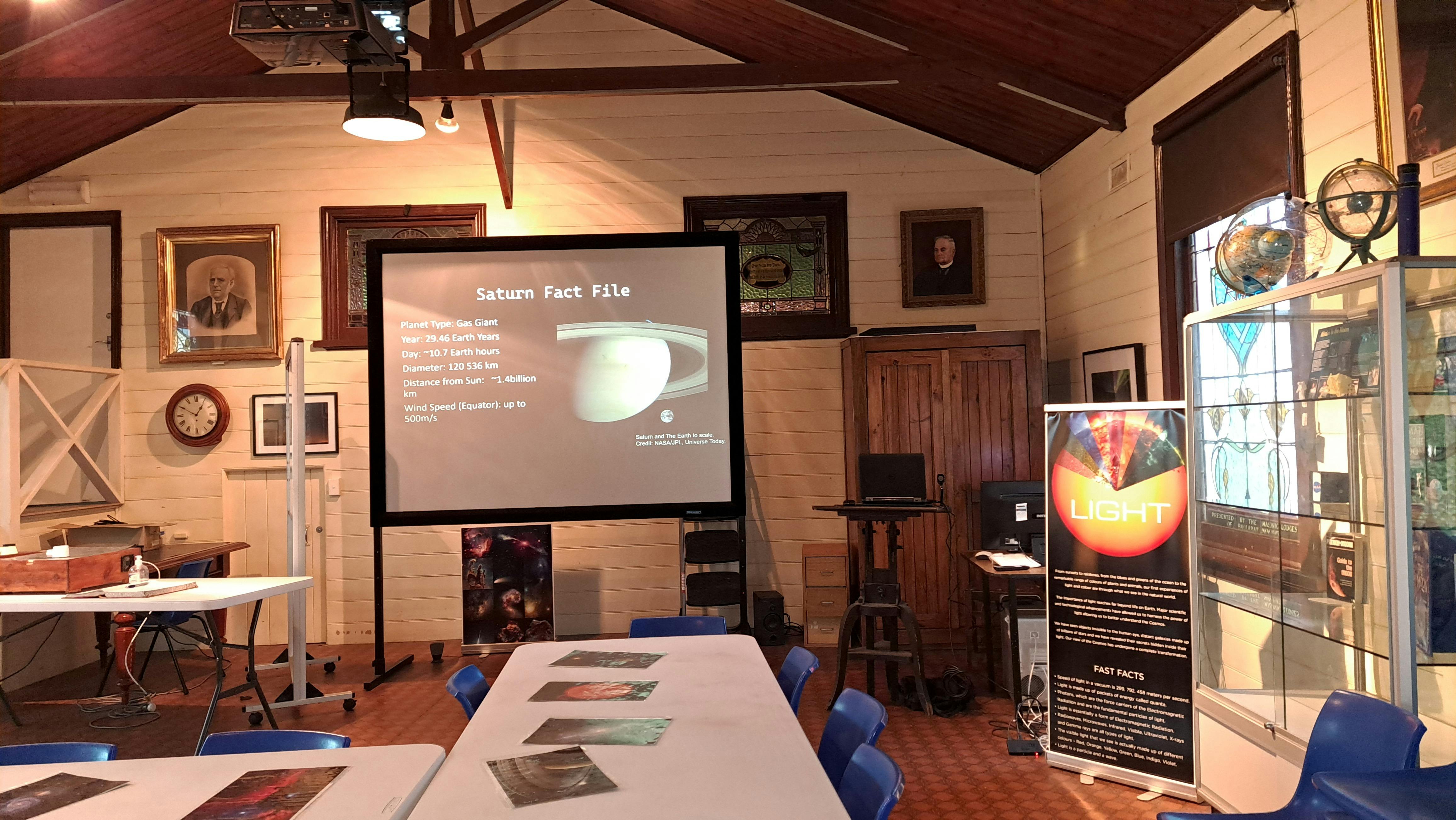 Photo of room with tables of photos of space around a screen with facts about space