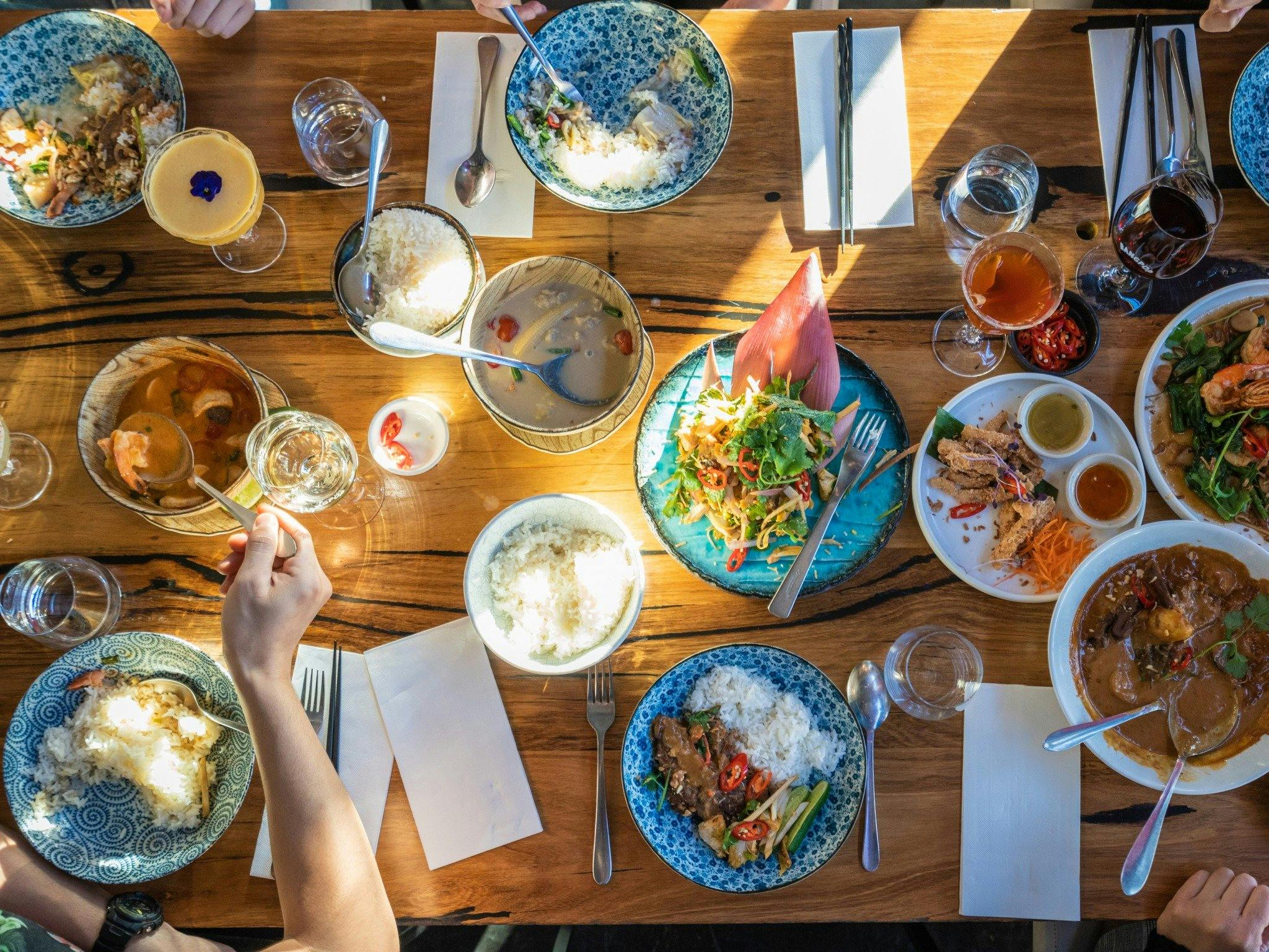 table full of Thai food and sharing plates with guests enjoying around it