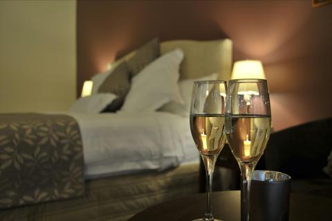 Two wine glasses placed on the side table next to a king bed