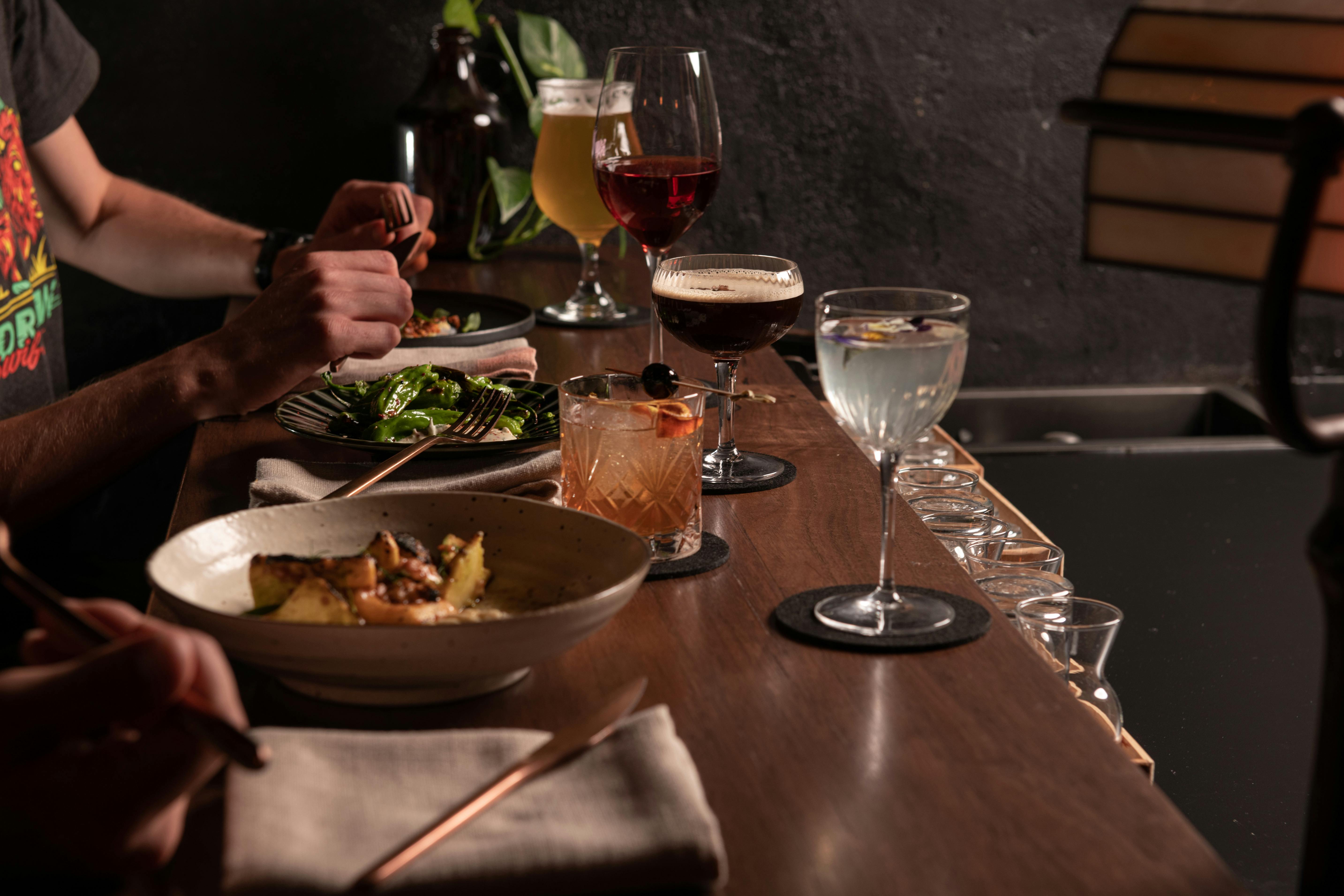 A group of people sitting at the bar with food and cocktails.