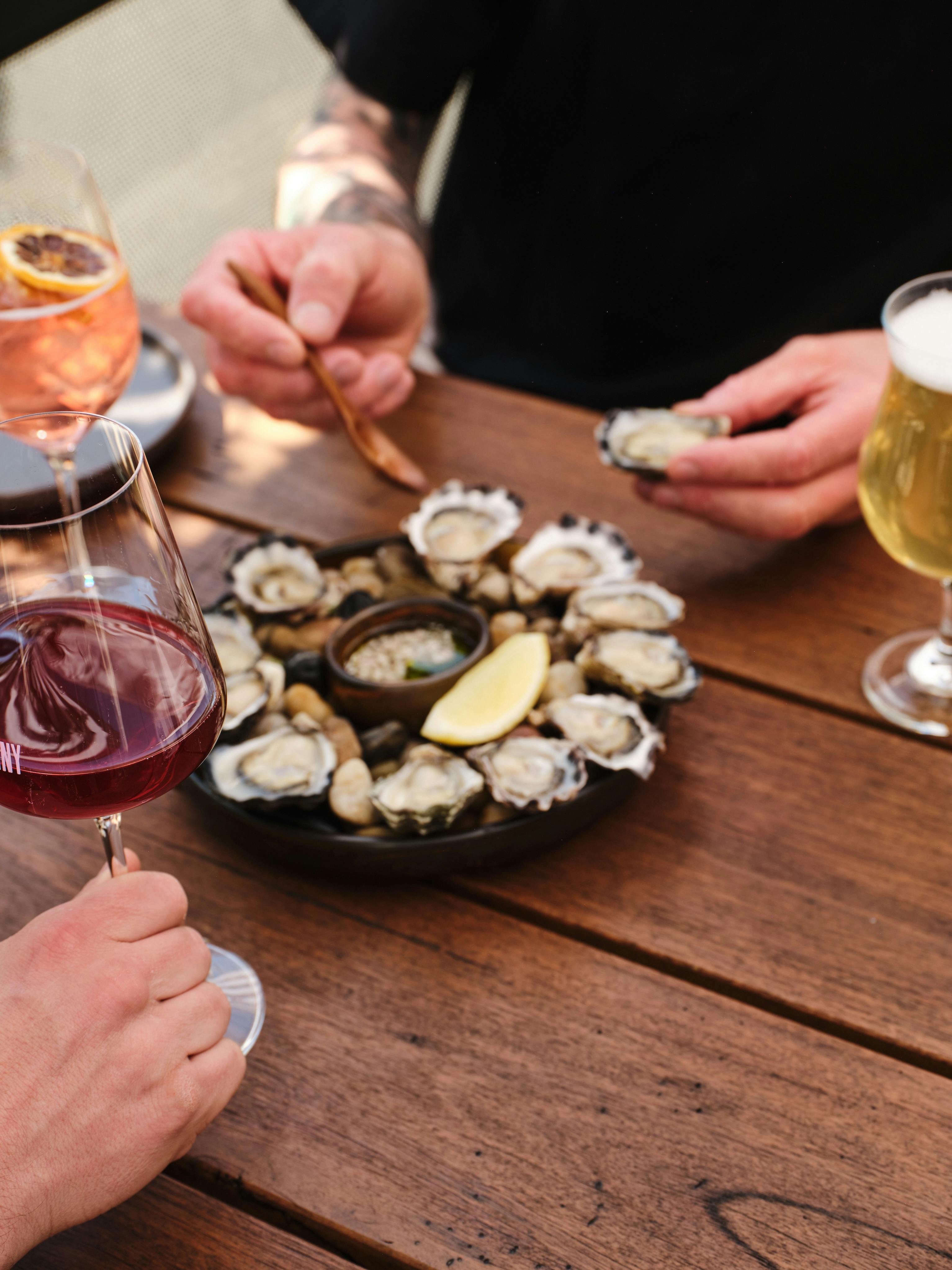 A group of people eating oysters and having wine at a table.