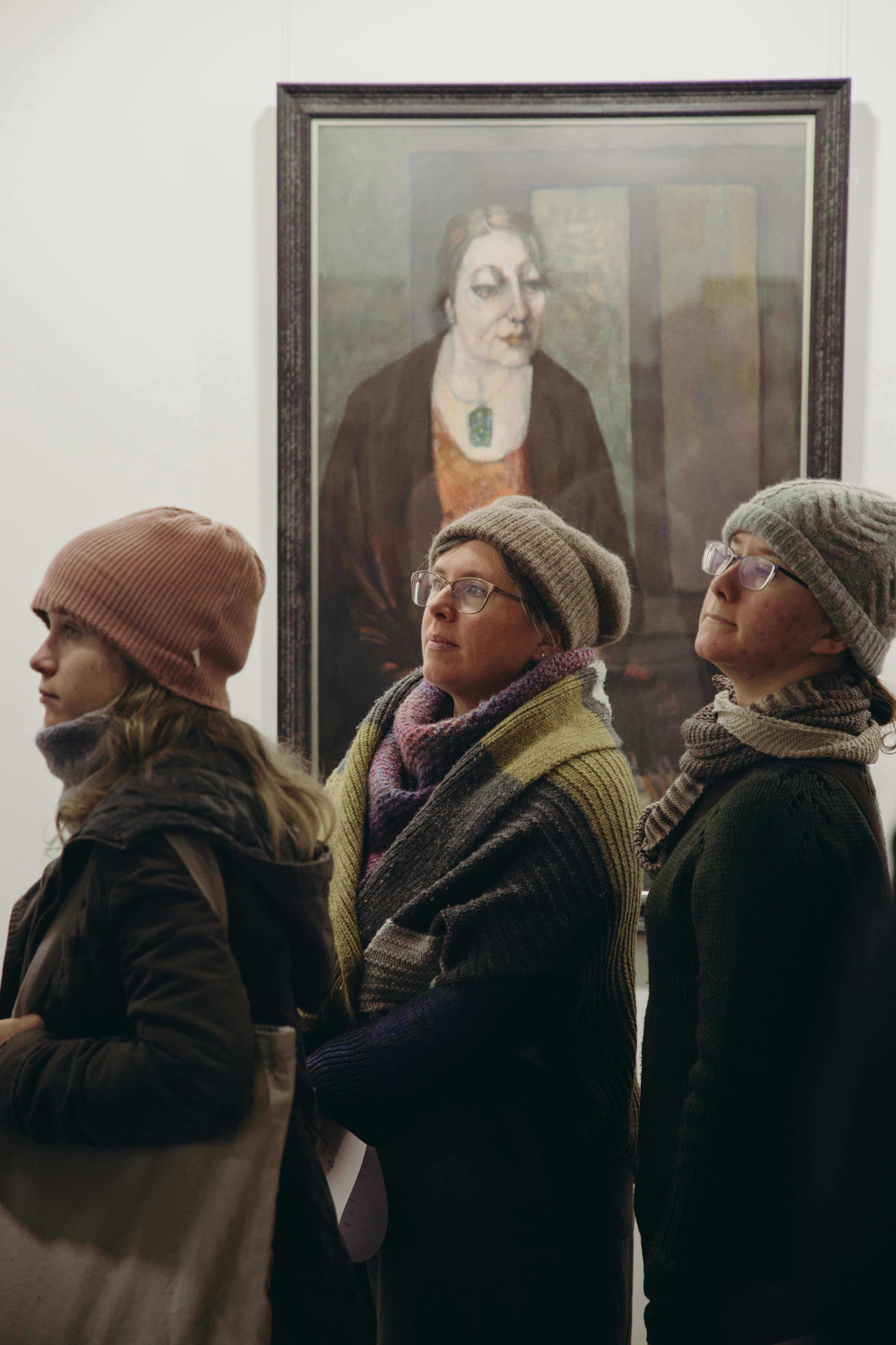 Three visitors at the Maldon Portrait Prize in front of a Norma Bailey Ramsey painting