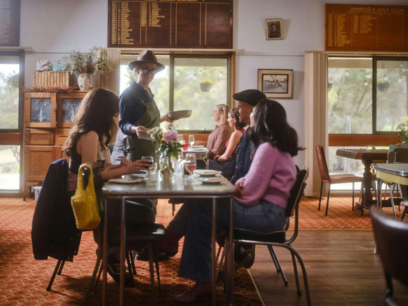 Group of people sitting in an old golf club dining room with the chef serving to tables
