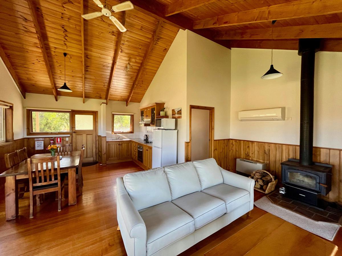 The living room  of Wattle Cottage featuring a dining tables, chairs. sofa, kitchen and fireplace