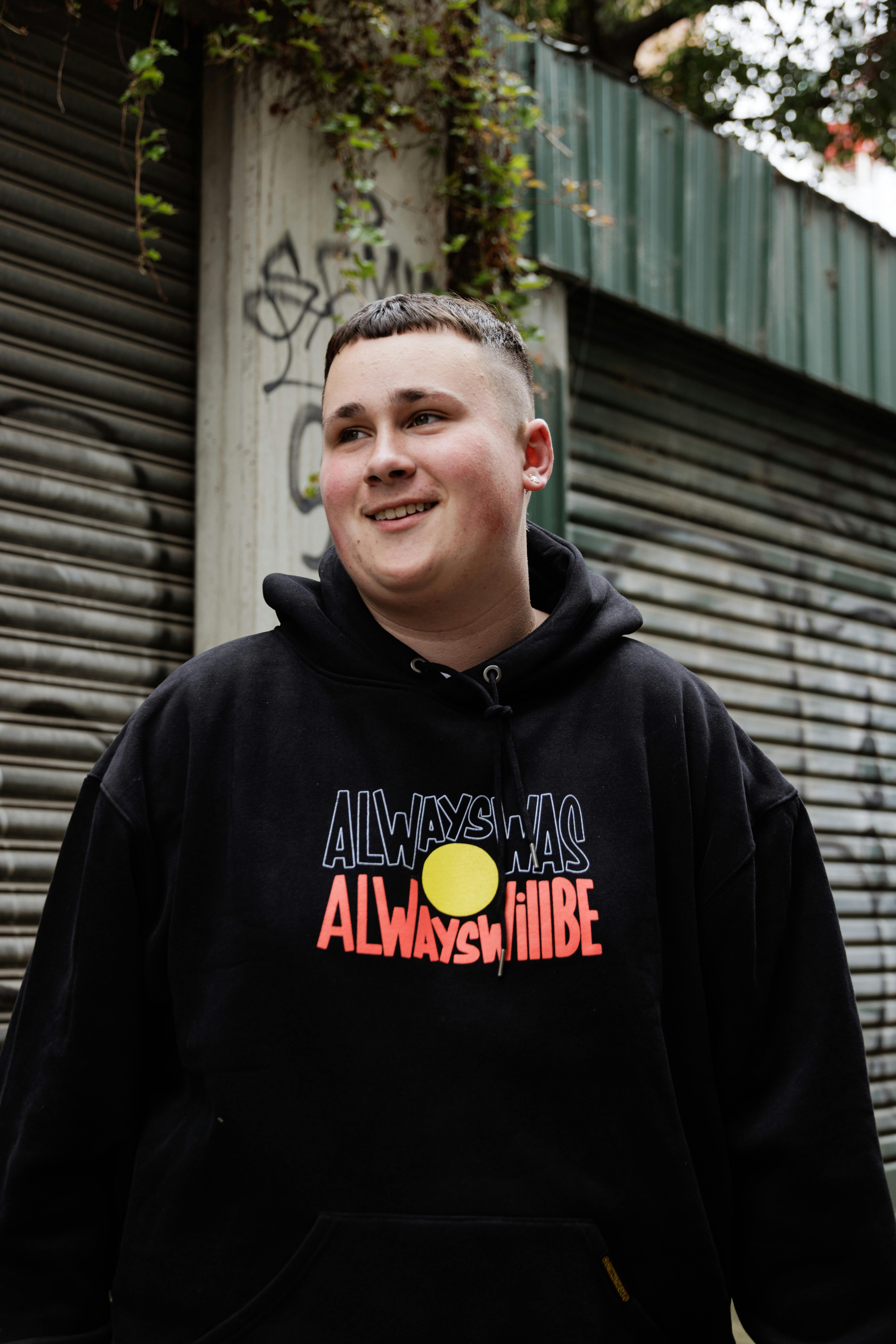 a person wearing a always was always will be hoodie in a laneway