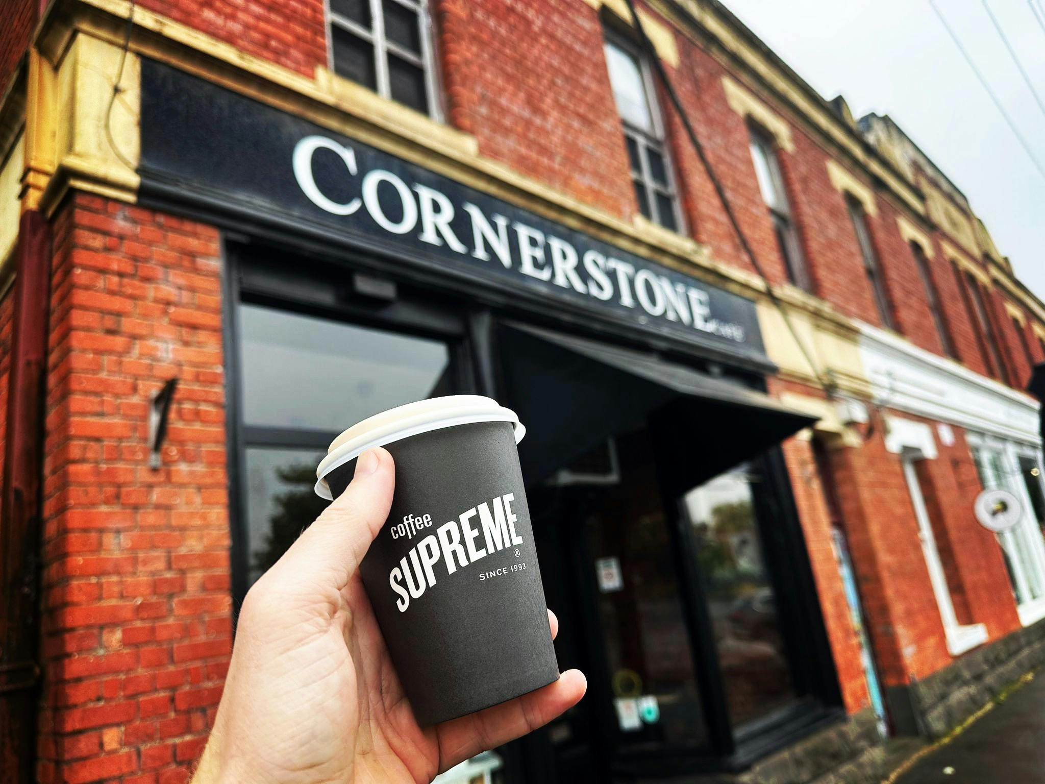 a hand holding a take away coffee in front of a cafe