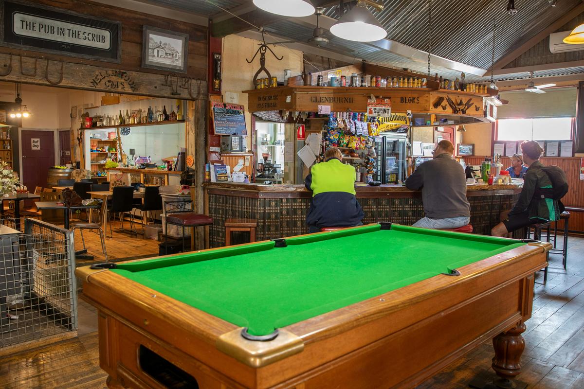 Large billiard table in the foreground with people sitting at a bar in the background