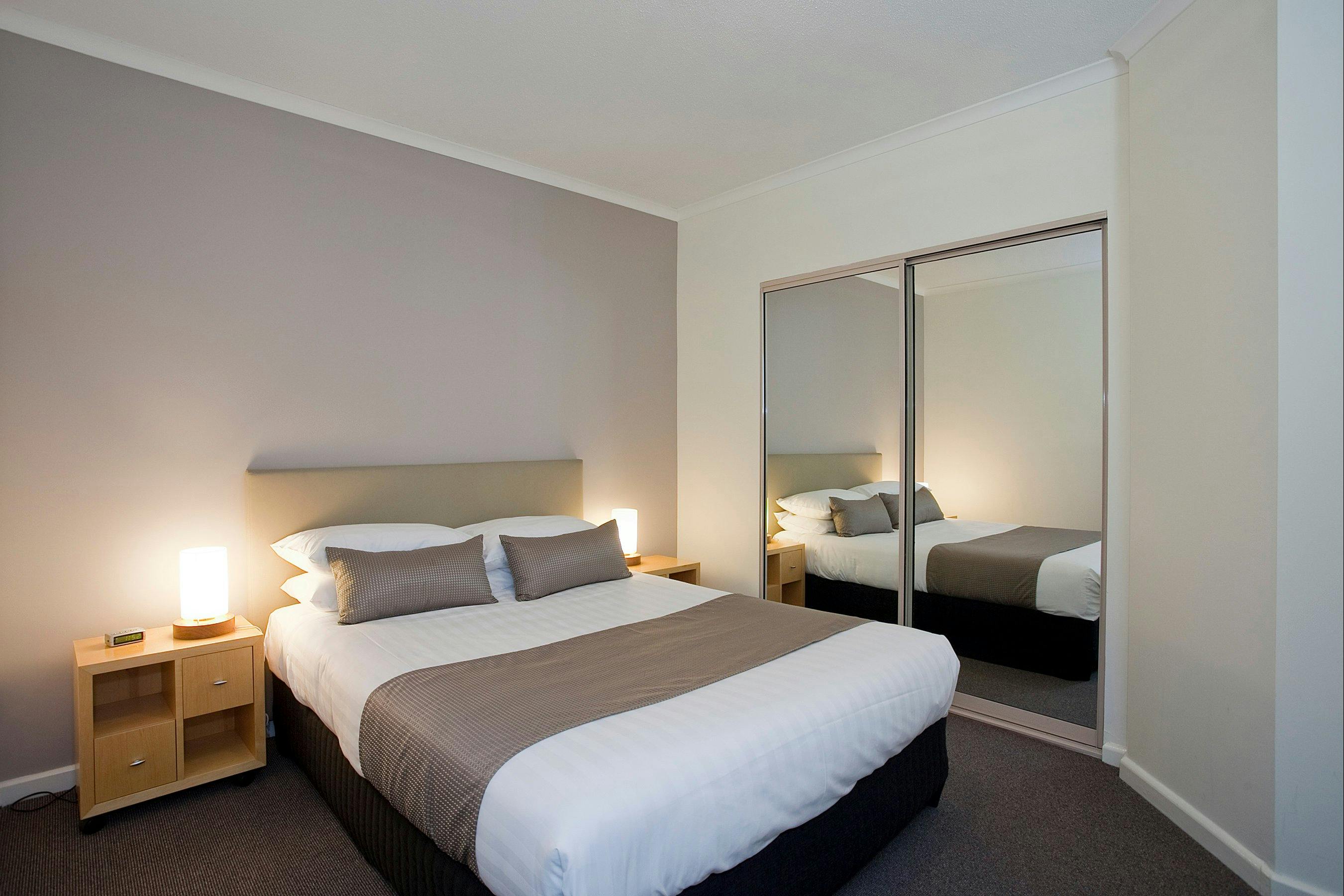 Apartment main bedroom showing queen, side tables and glass fronted wardrobe.