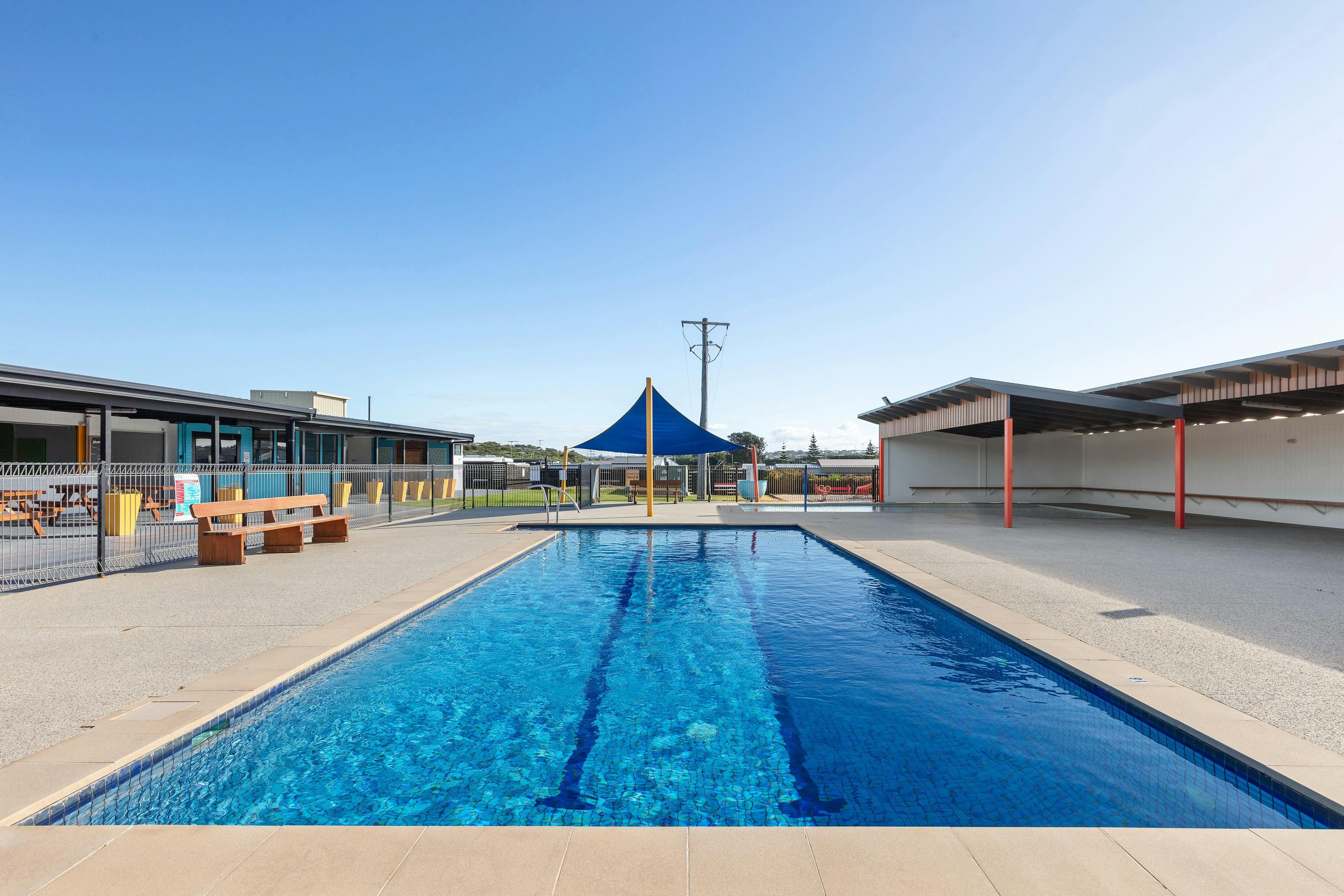 Outdoor pool with seating and shade at Collendina Holiday Park on a sunny day.