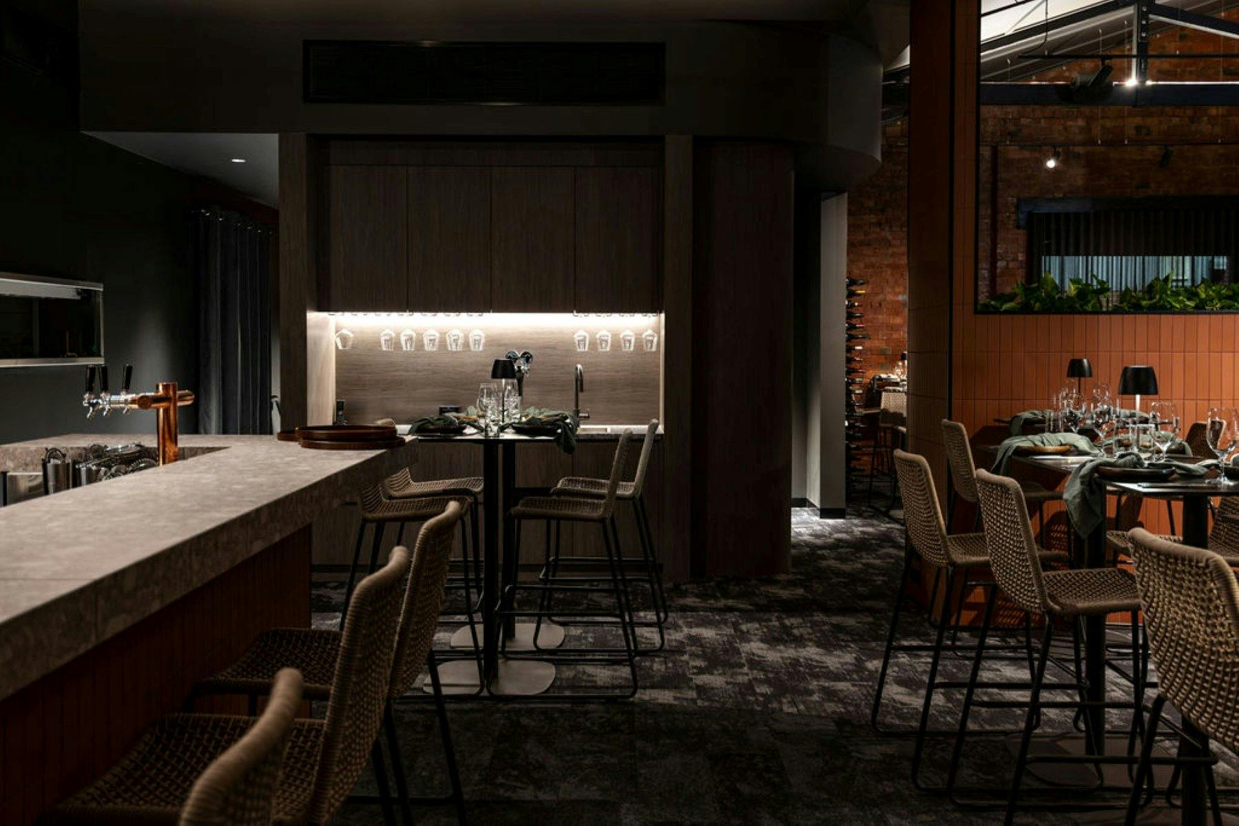interior of a restaurant with black carpet and walls and chairs at the bar and tables with glasses