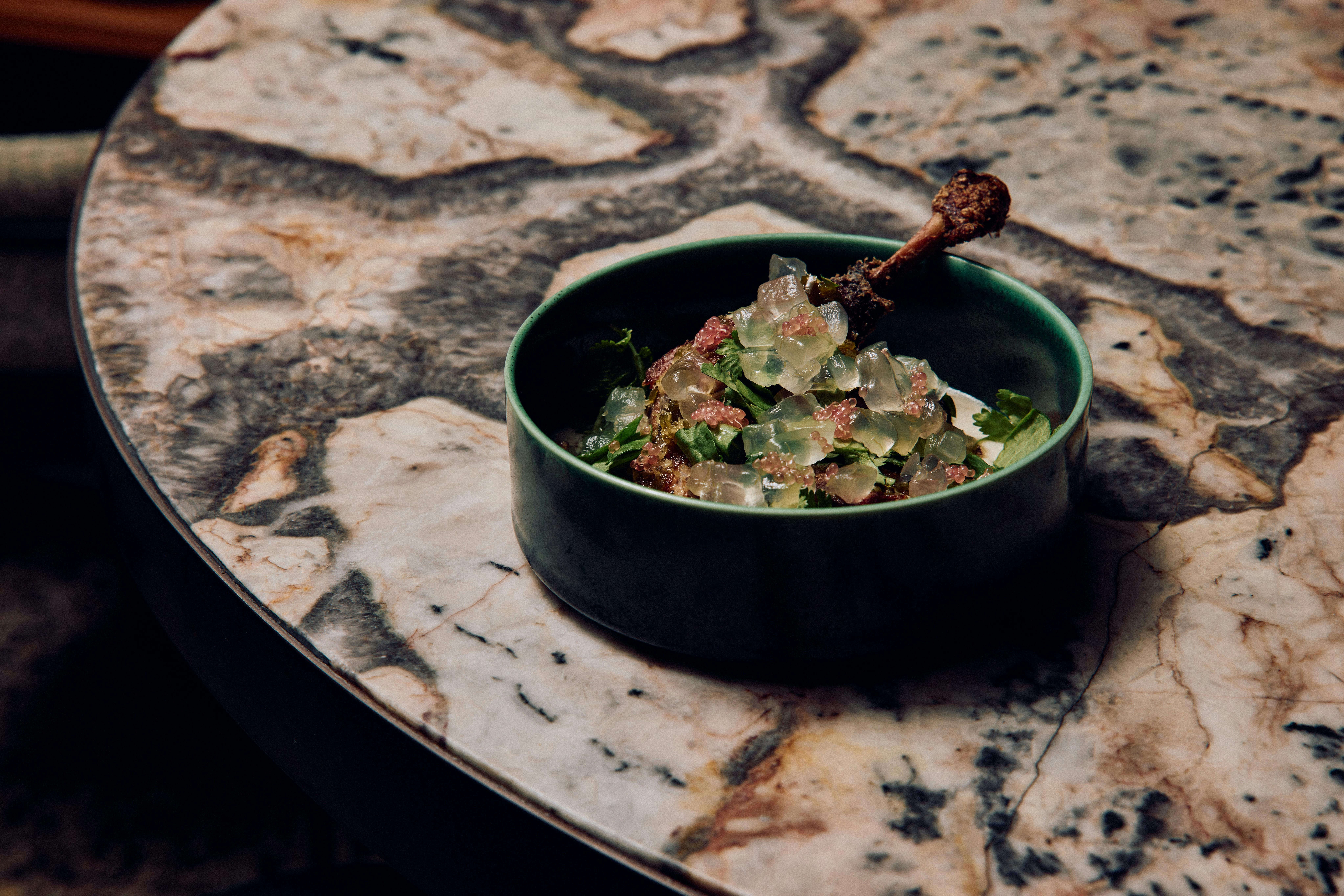 A blue bowl holding a dish of slow-cooked duck leg
