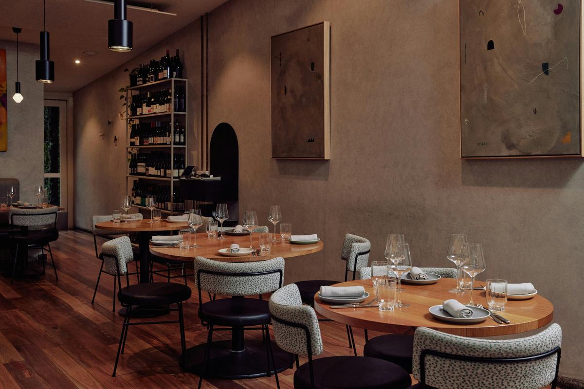 A restaurant dining room with wooden tables, comfy plush chairs and soft grey walls