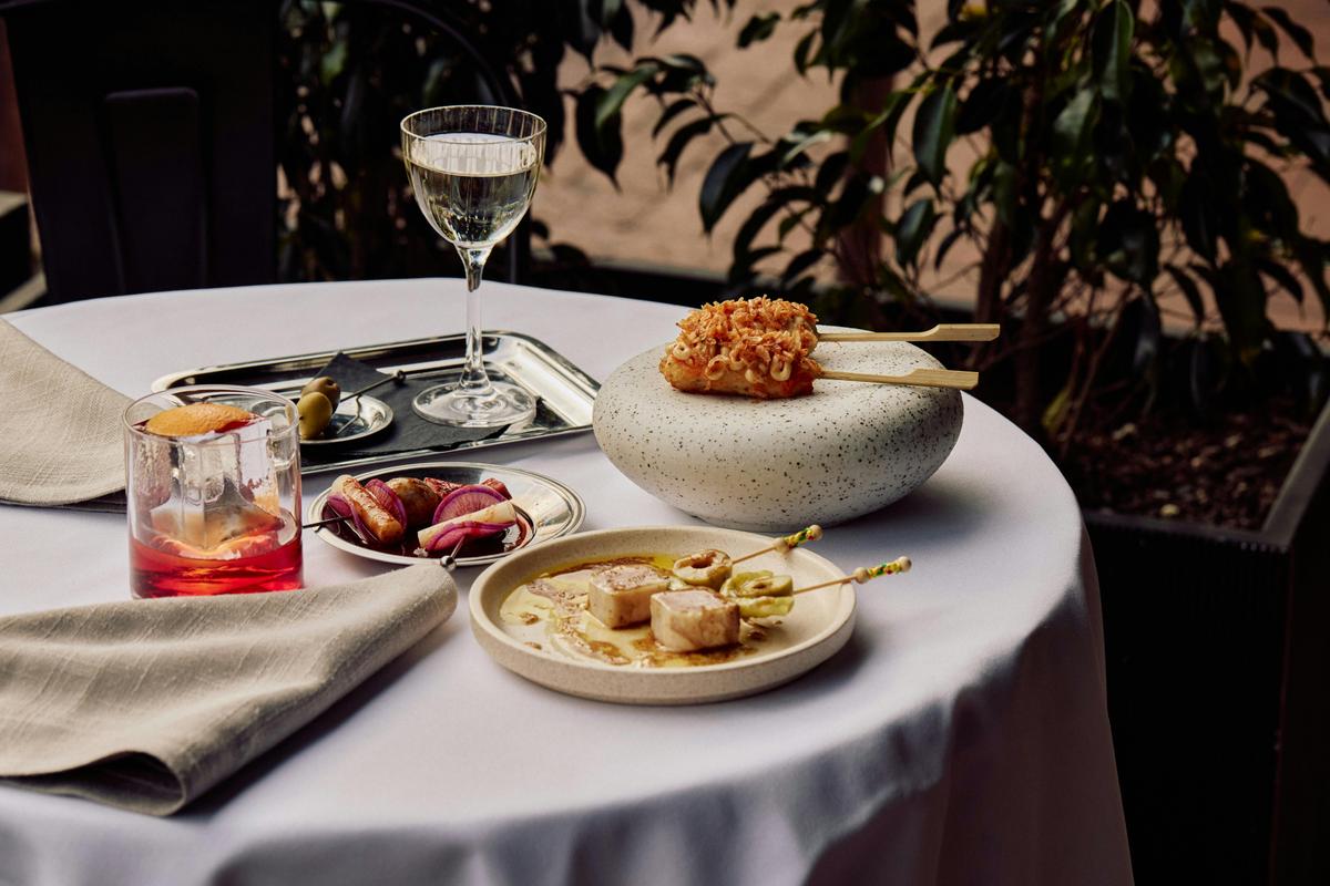 A series of skewered meats and seafood alongside two cocktails on a white-clothed table