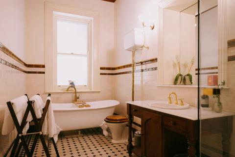 A vintage-style bathroom featuring a clawfoot tub, brass taps, a wooden vanity, and classic tiling.