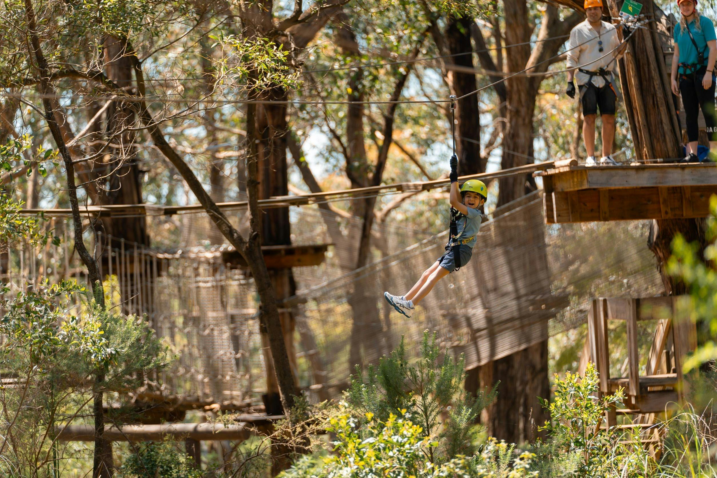 Small child in harness & safety gear going down a zipline from a high ropes obstacles course