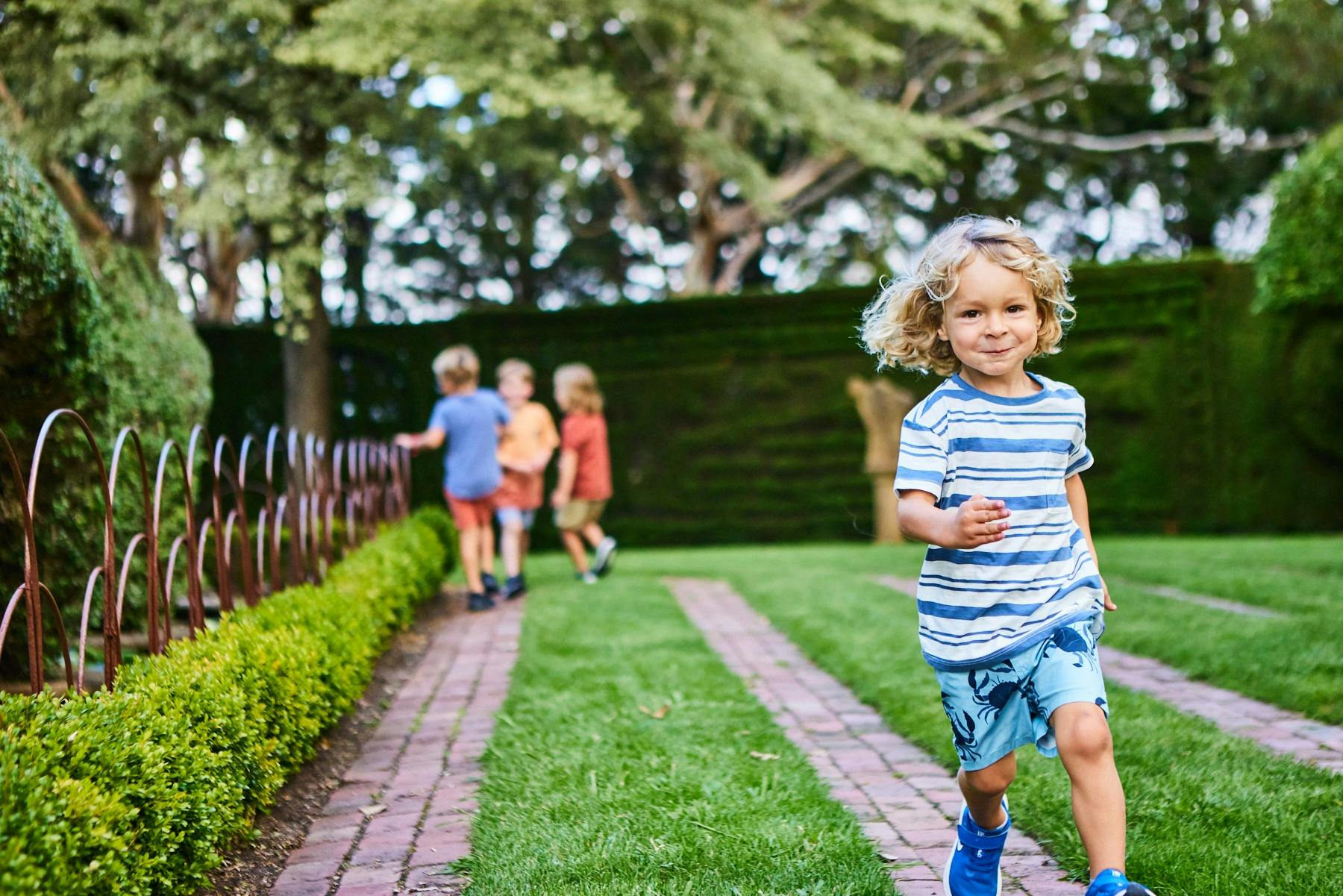 Group of small children running around a turf maze, one small children running and smiling at camera