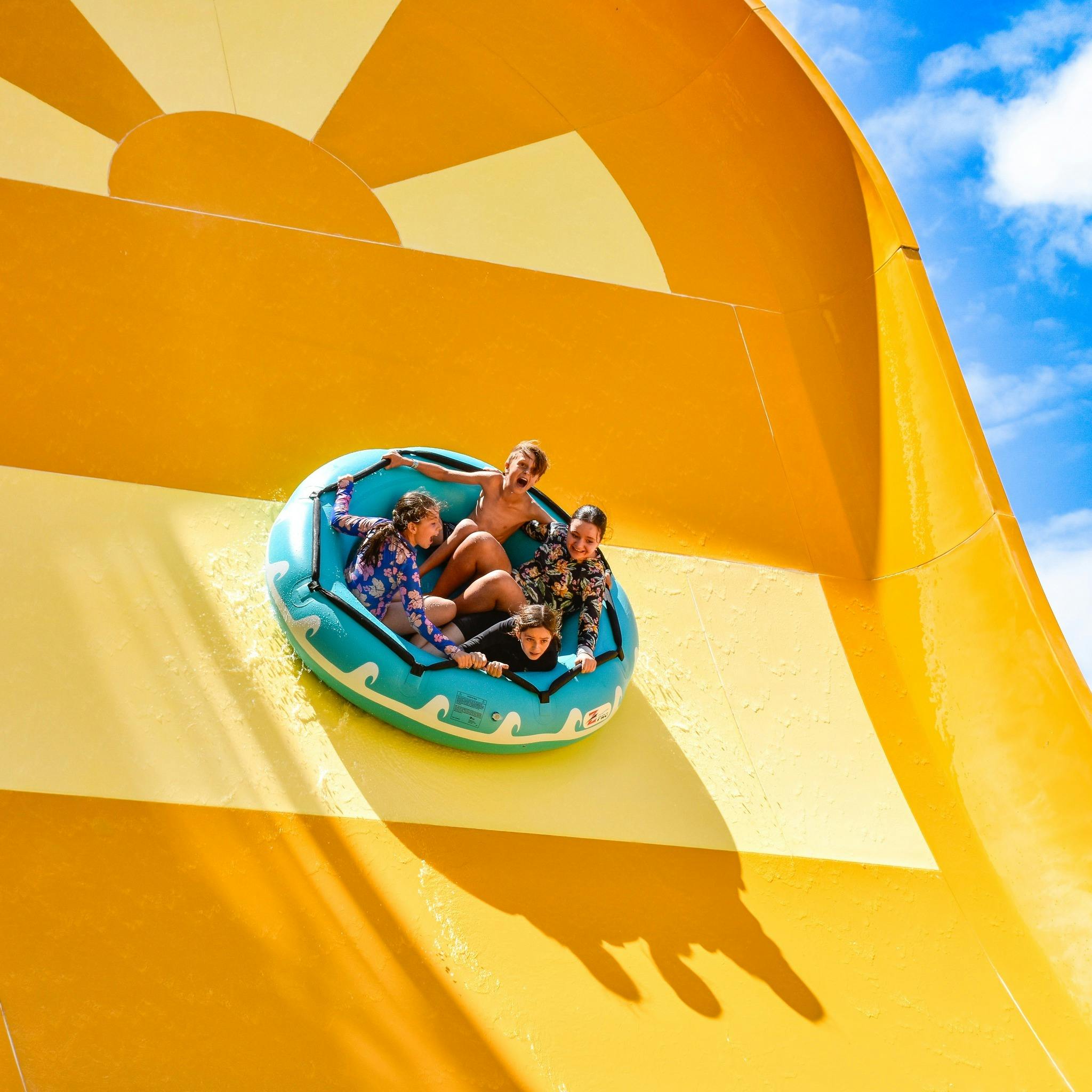 Four children in a raft on a water slide with huge smiles and having fun