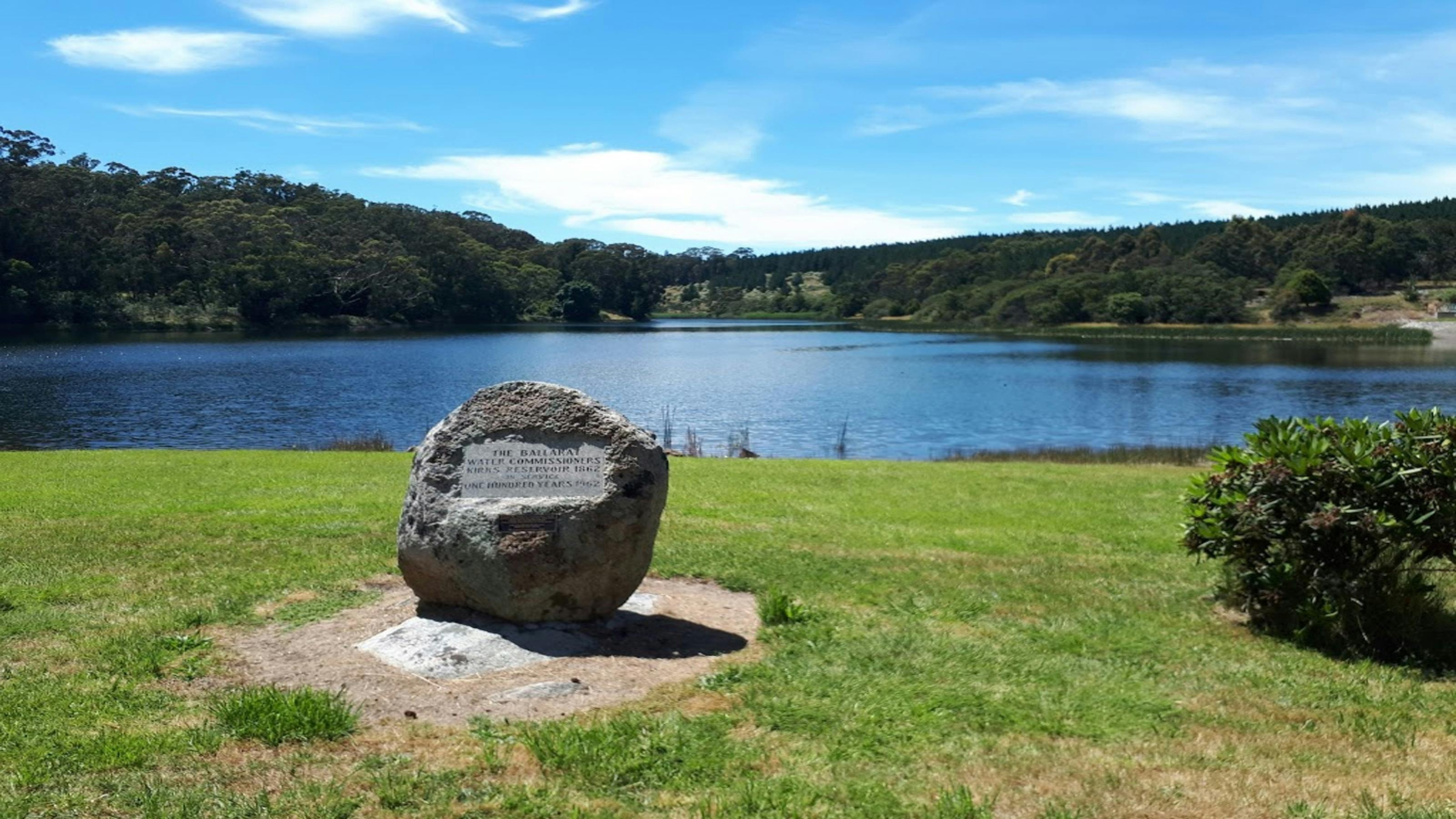 reservoir with trees in background with blue skies overhead and plague on rock in foreground
