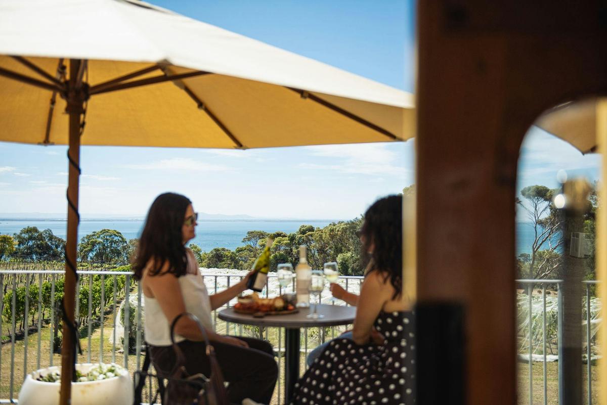 two people sitting under umbrella drinking wine with the ocean in the background