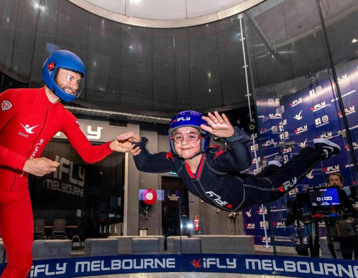 Young flyer supported by instructor during a family flight session at iFLY Melbourne.