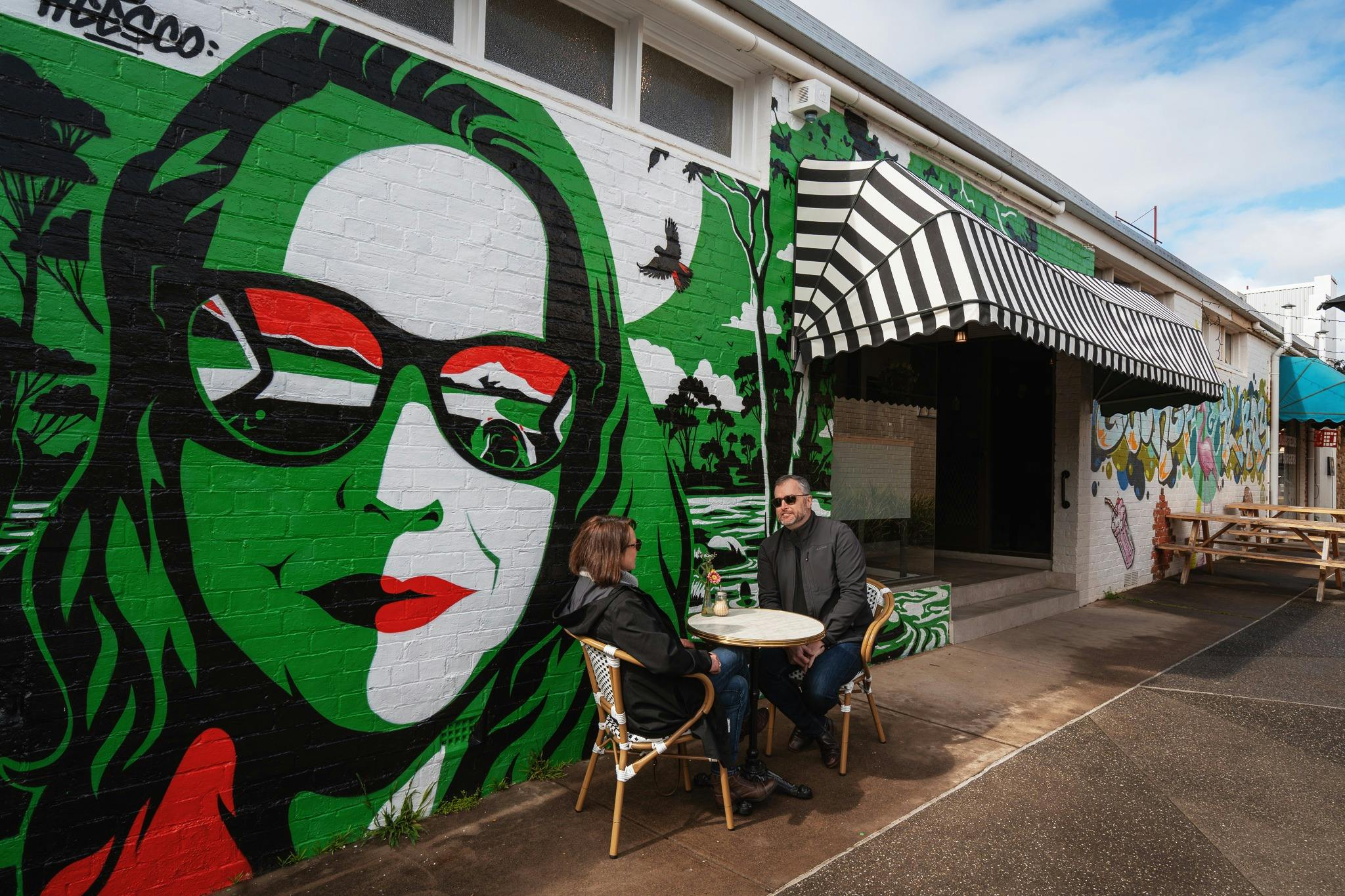 A mural with a woman with green hair and sunglasses with red, green, white and black in the frames