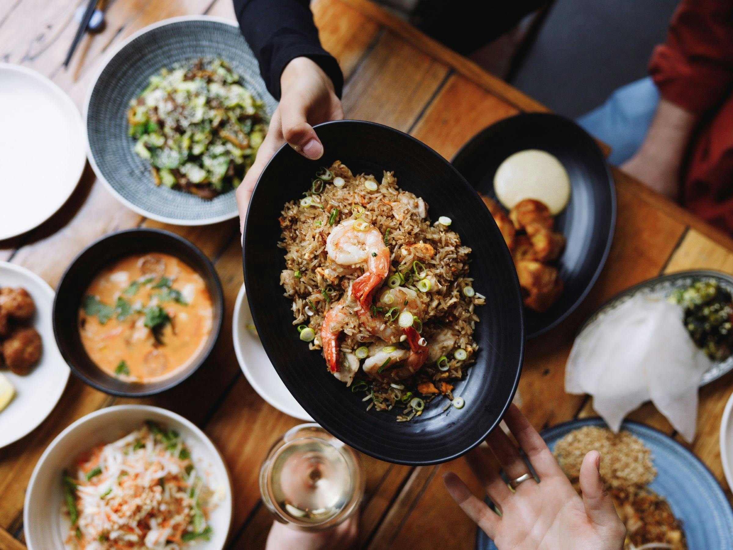 A variety of South East Asian dishes on the table with fried rice being passed across the table