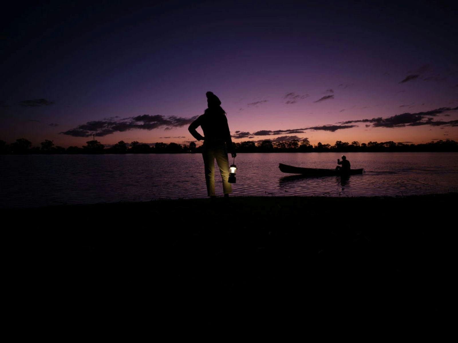 Person holding a lantern at dusk and watching a person in a canoe on the lake