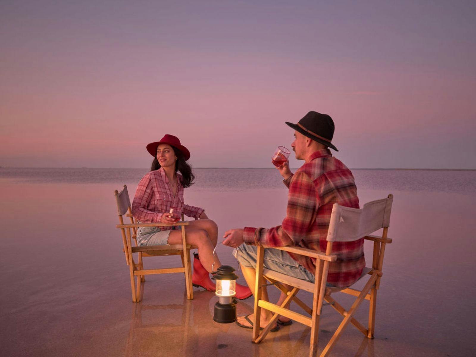 Two people sitting on chairs on a salt lake with a lantern