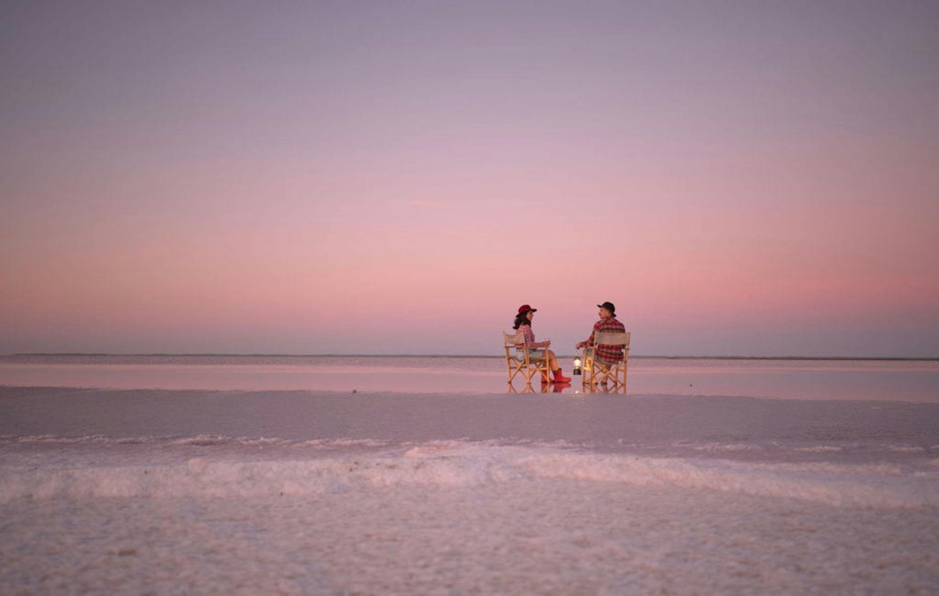 Two people sitting on chairs on a salt lake that appears pink
