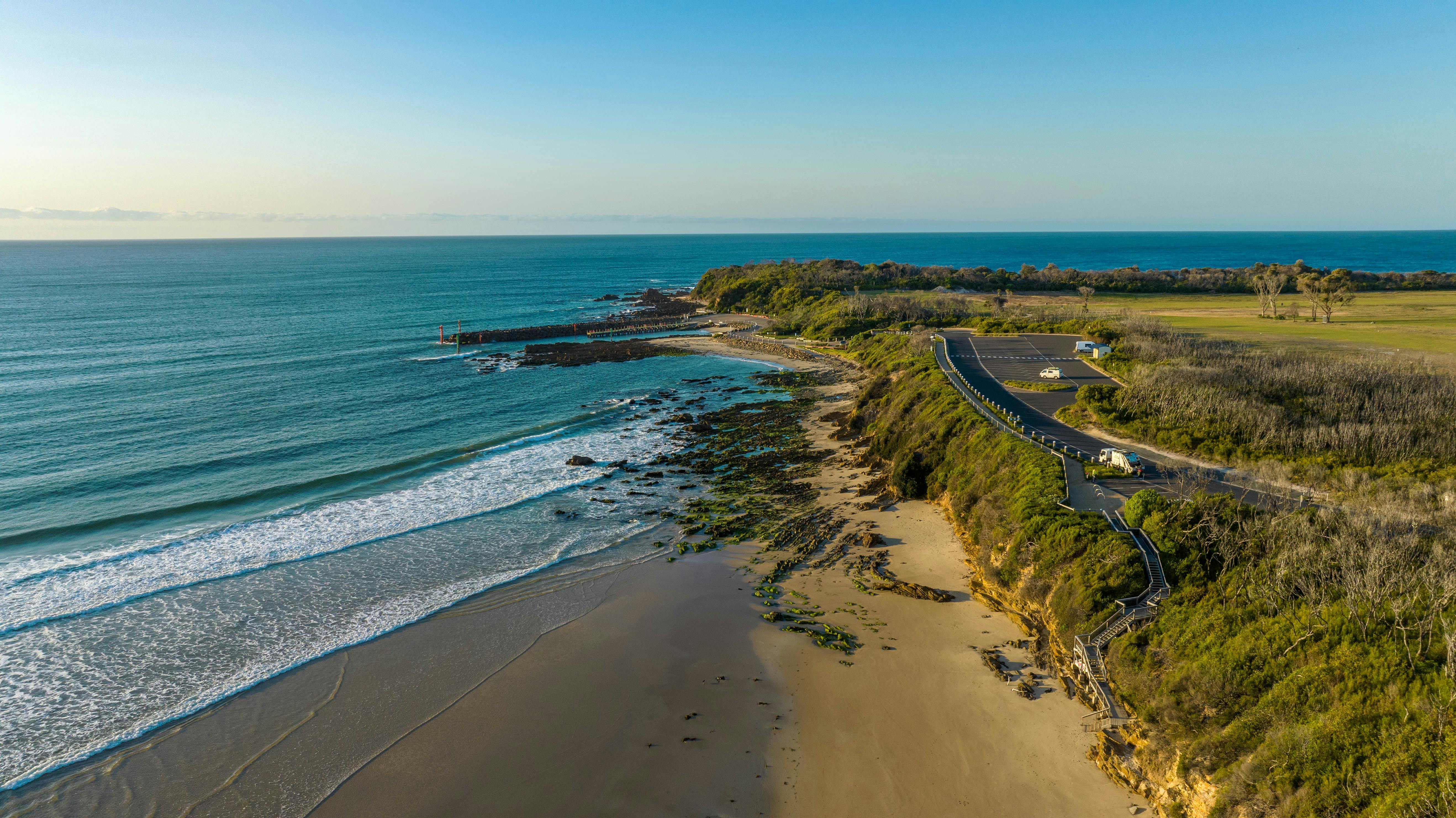 View of the sea with carpark and walkway with stairs leading down to beach with waves breaking