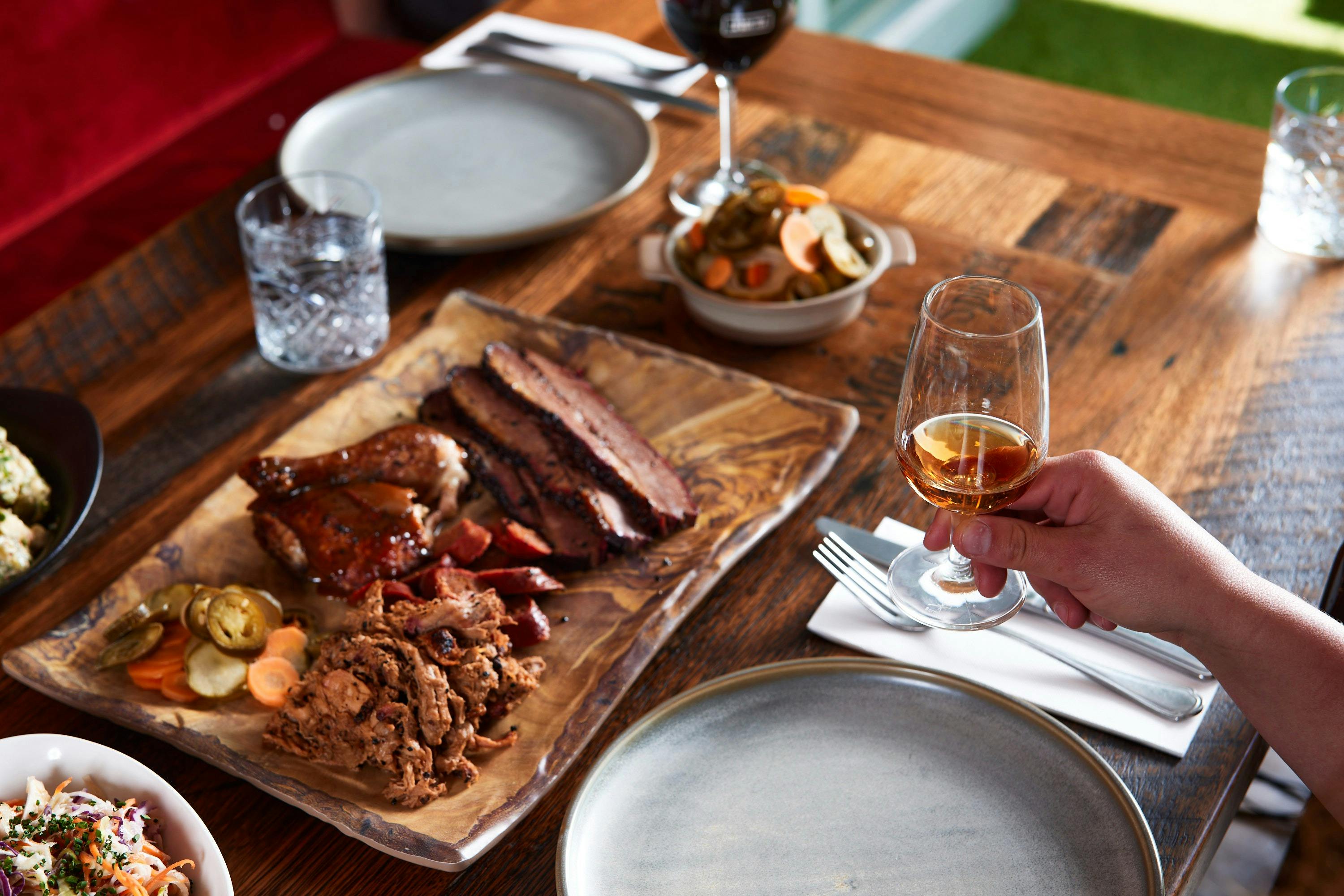 barbeque meats on a tray with someone holding a glass of wine