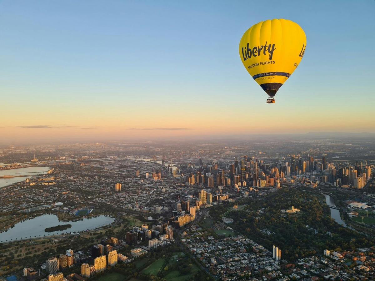 Yellow branded hot air balloon floating over Melbourne city skyline