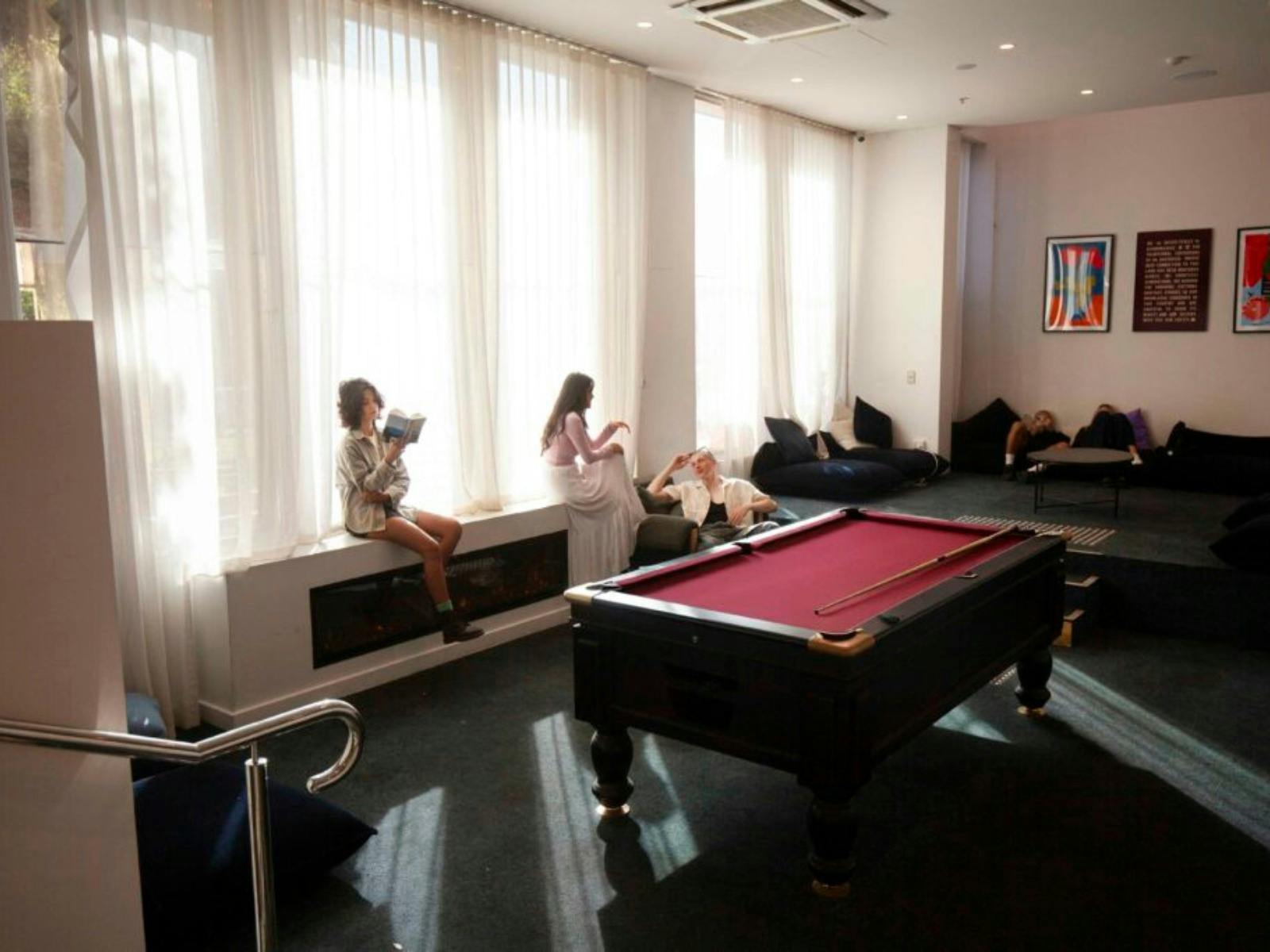 one person reading a book and two other talking to each other, pool table and some seats