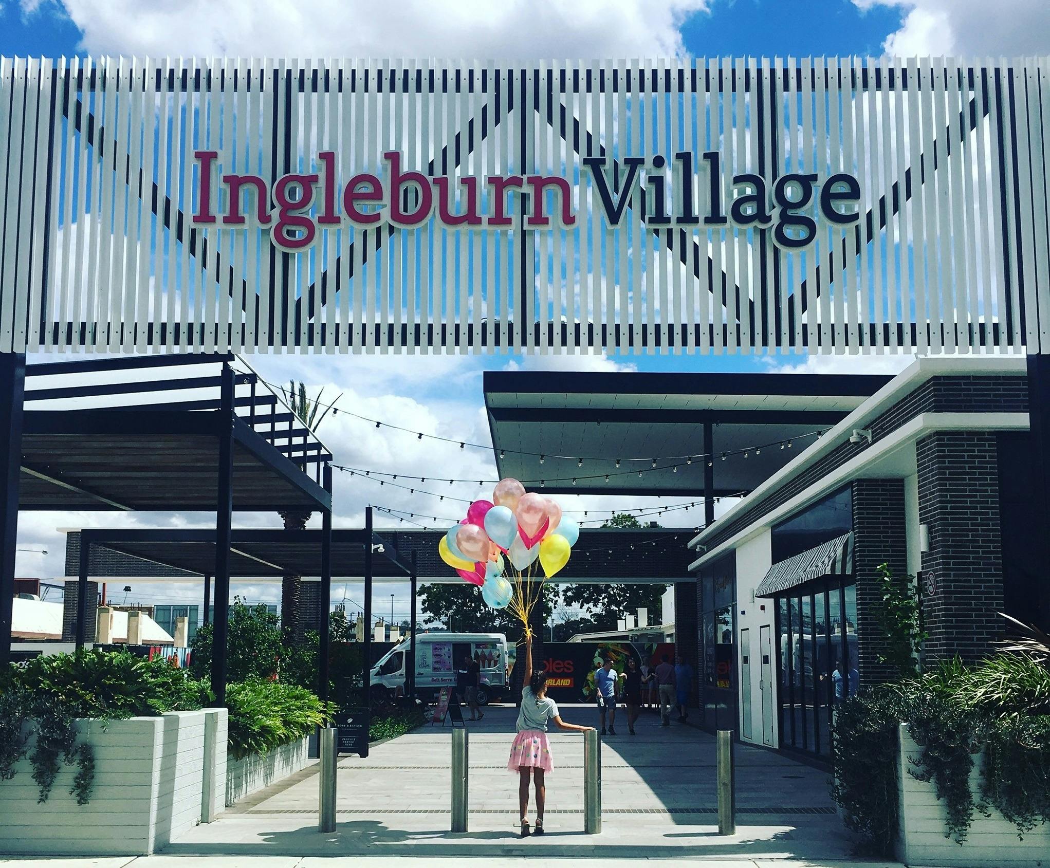 Girl standing with balloons in front of Ingleburn Village sign