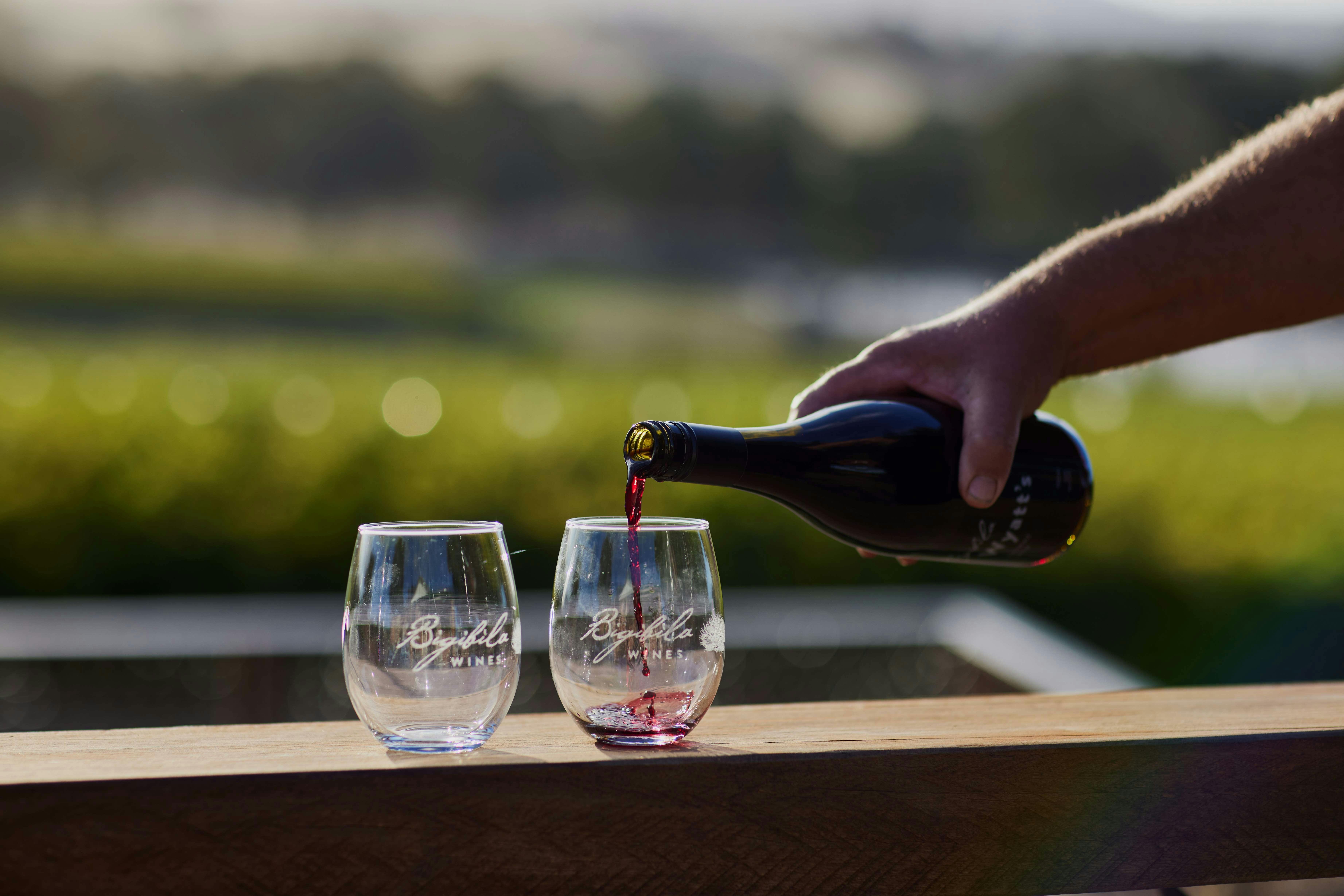 A hand is reaching into frame, holding a bottle of wine and pouring it into two wine glasses