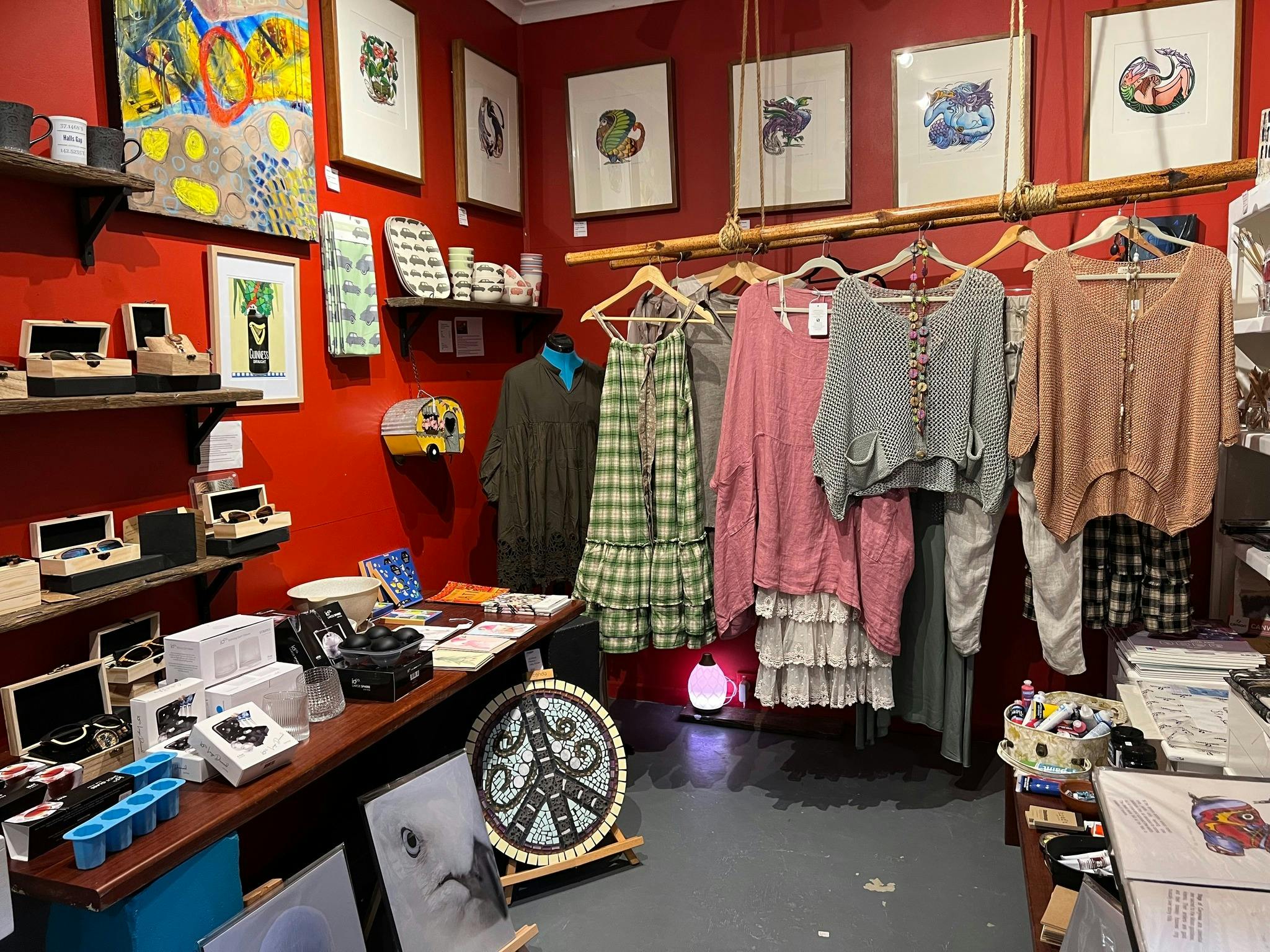 Corner of a gallery with clothing and various artworks for sale