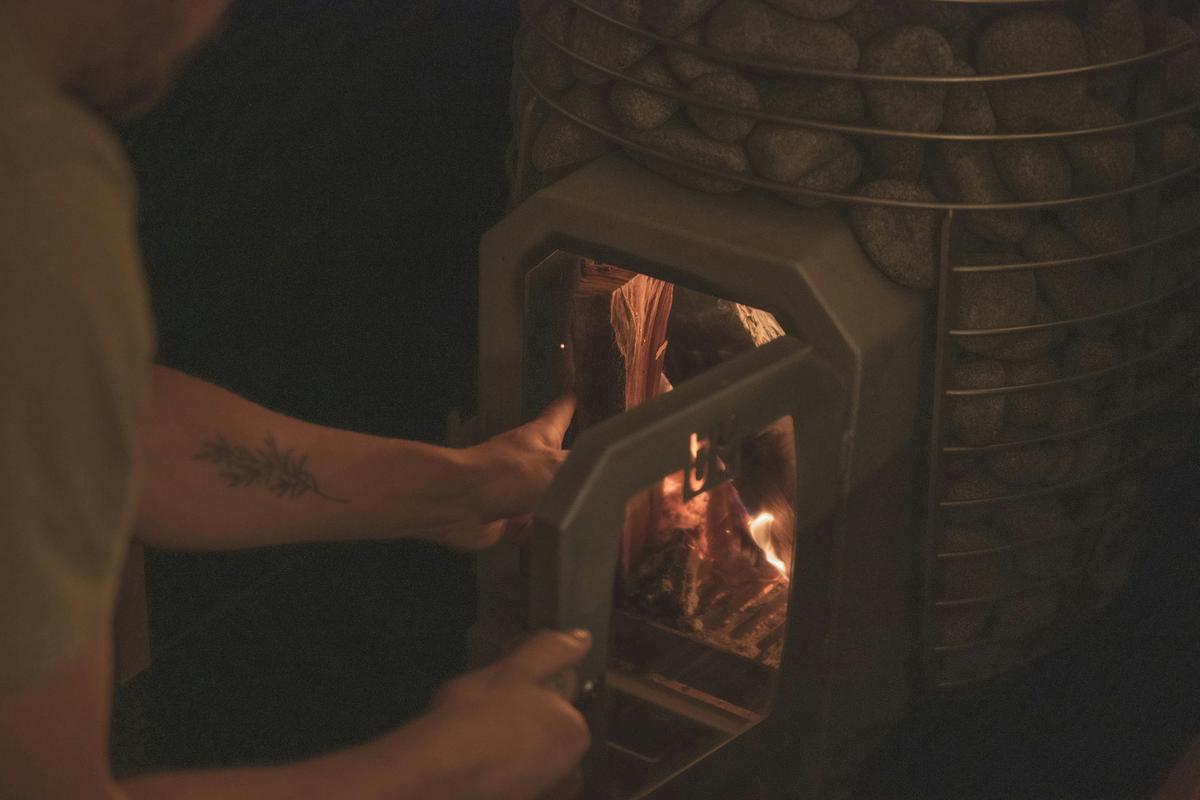 Loading wood into a wood fired Huum sauna heater in  dim lighting