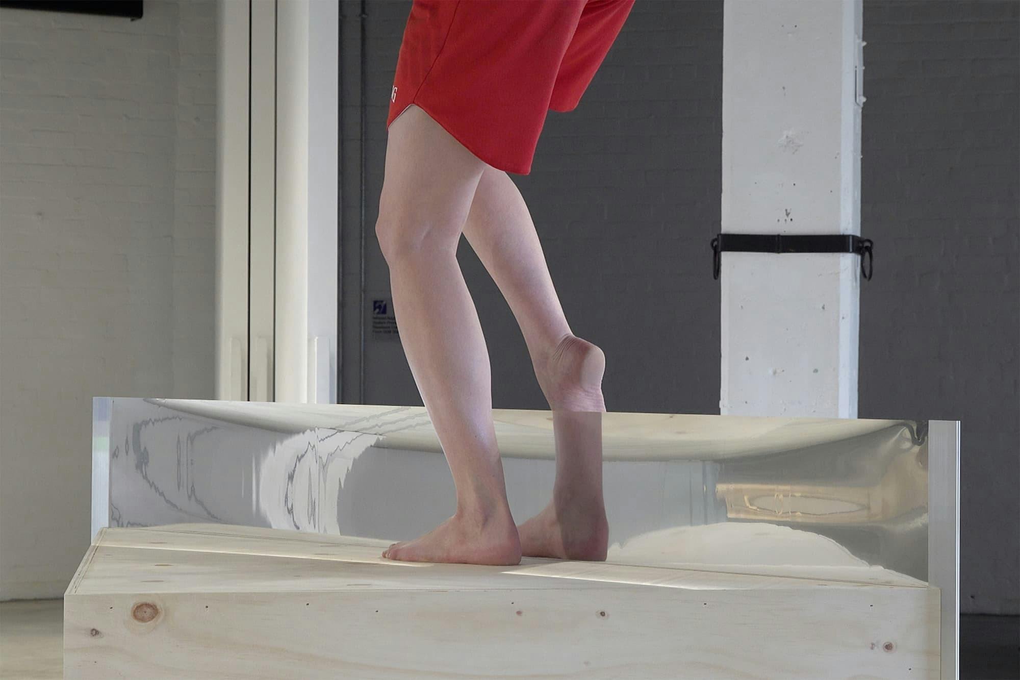 Artist steps on plinth with mirrored plank in between their feet.