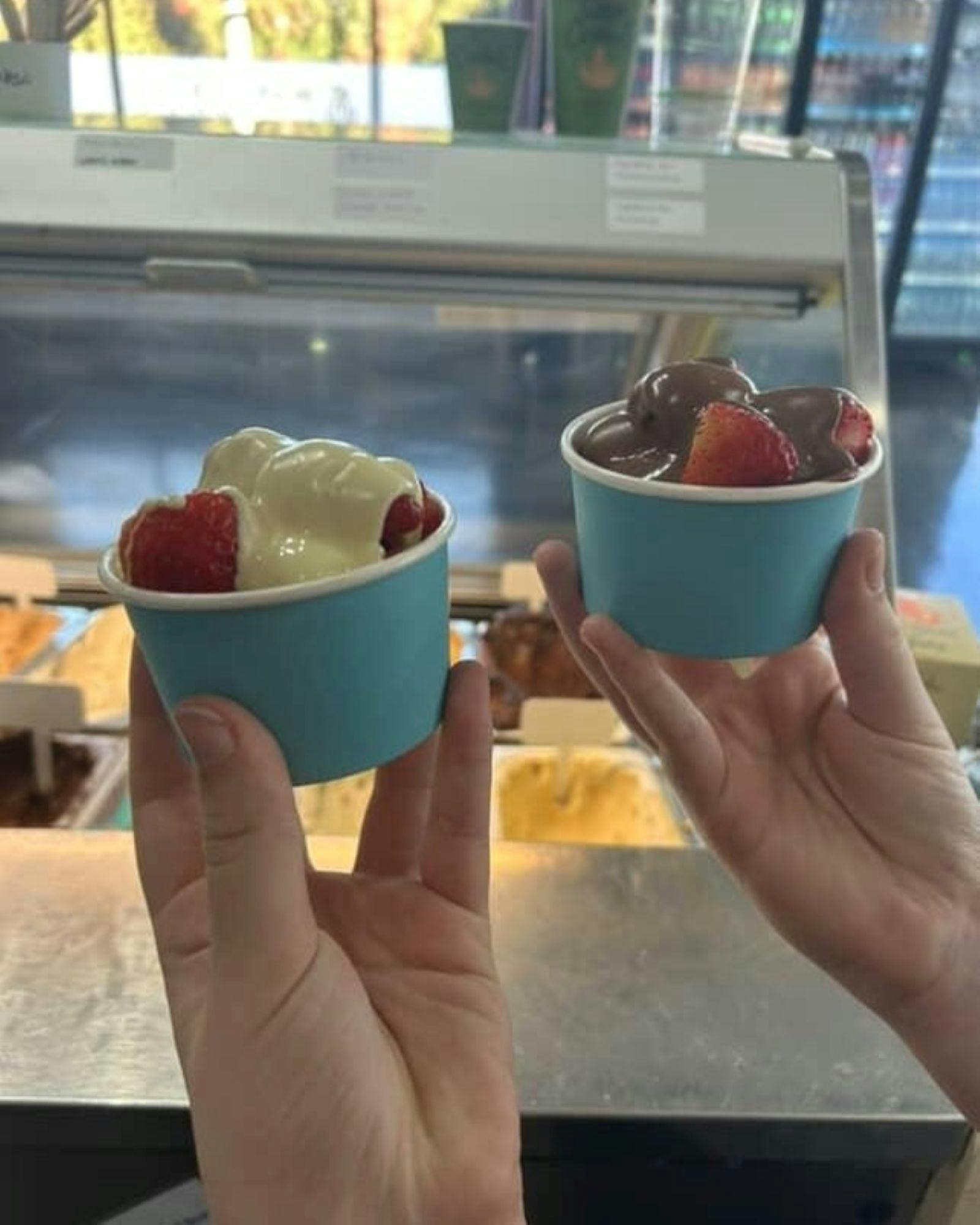 Two small tubs of strawberries with chocolate drizzled over them