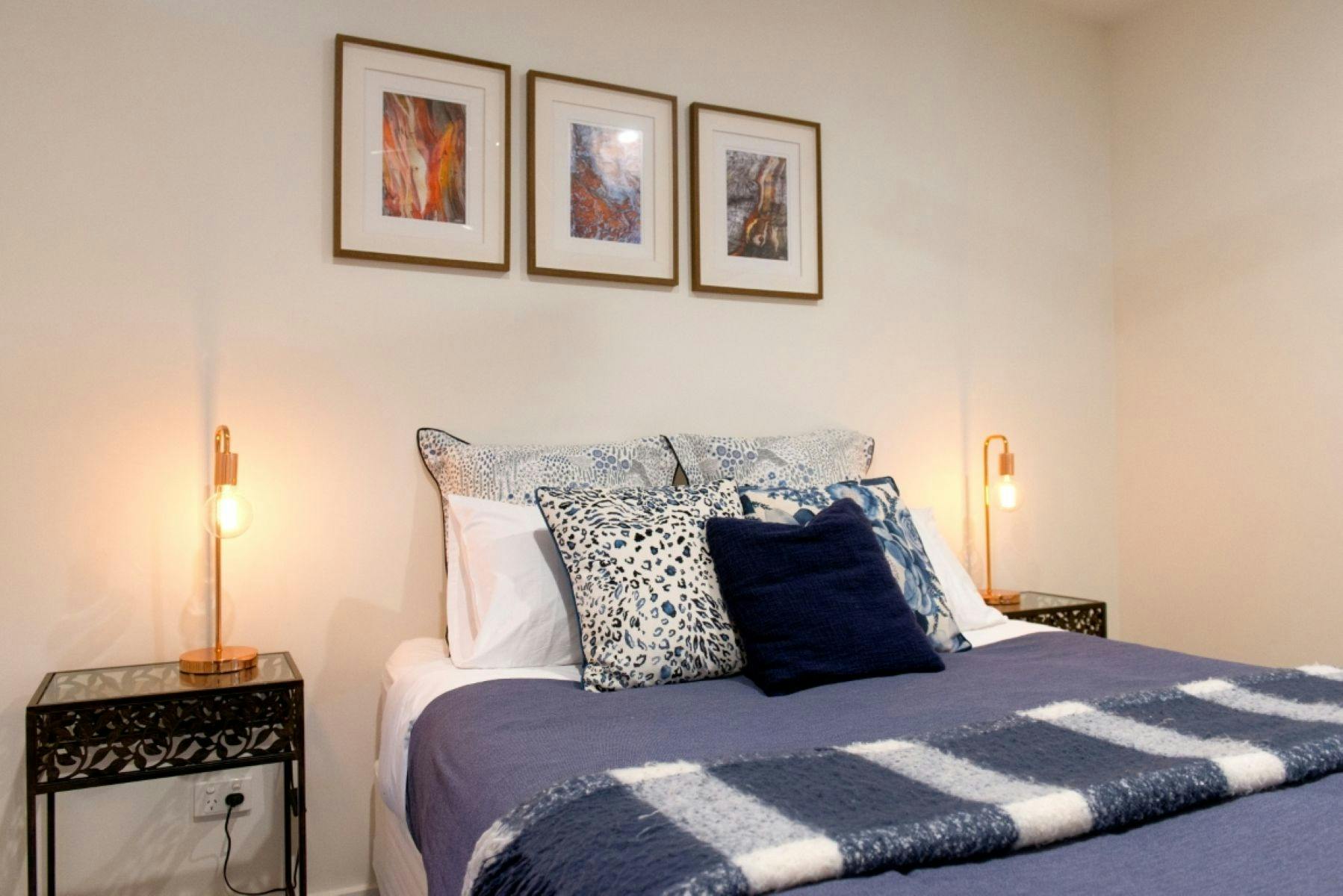 Bedroom two with a bed, three paintings above and side tables either side