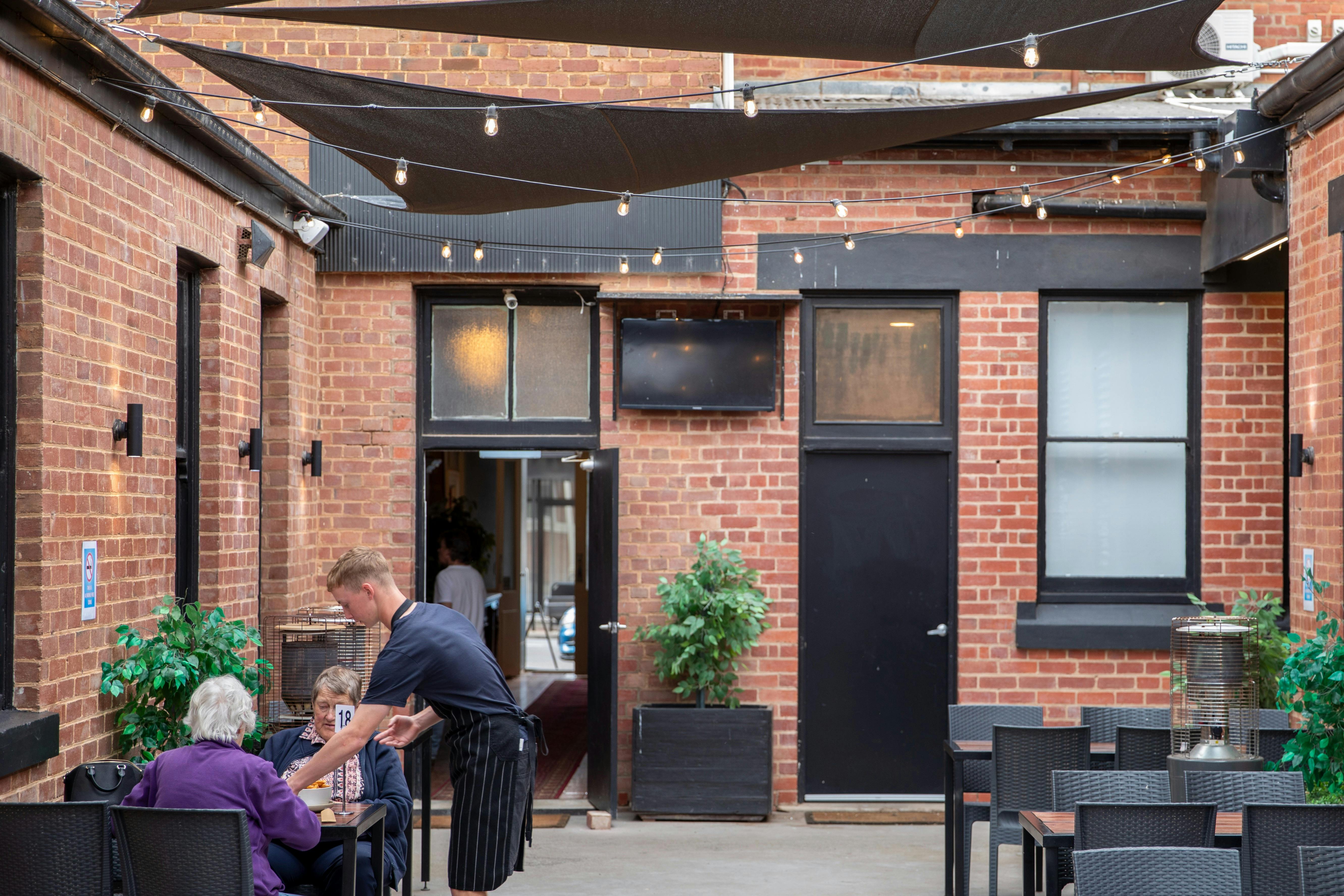Person serving two people at a table in an open courtyard