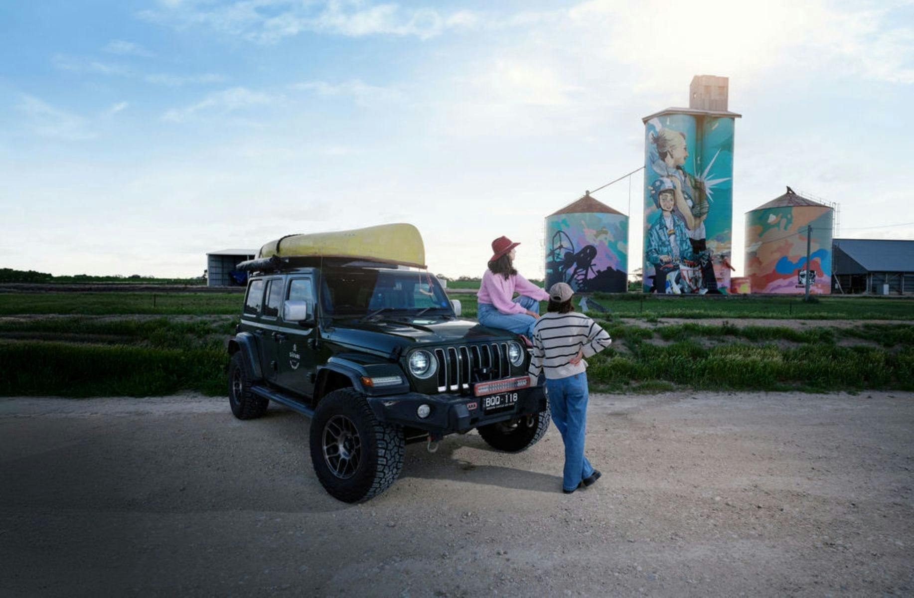 Person standing in front of a Jeep with painted silos in the background
