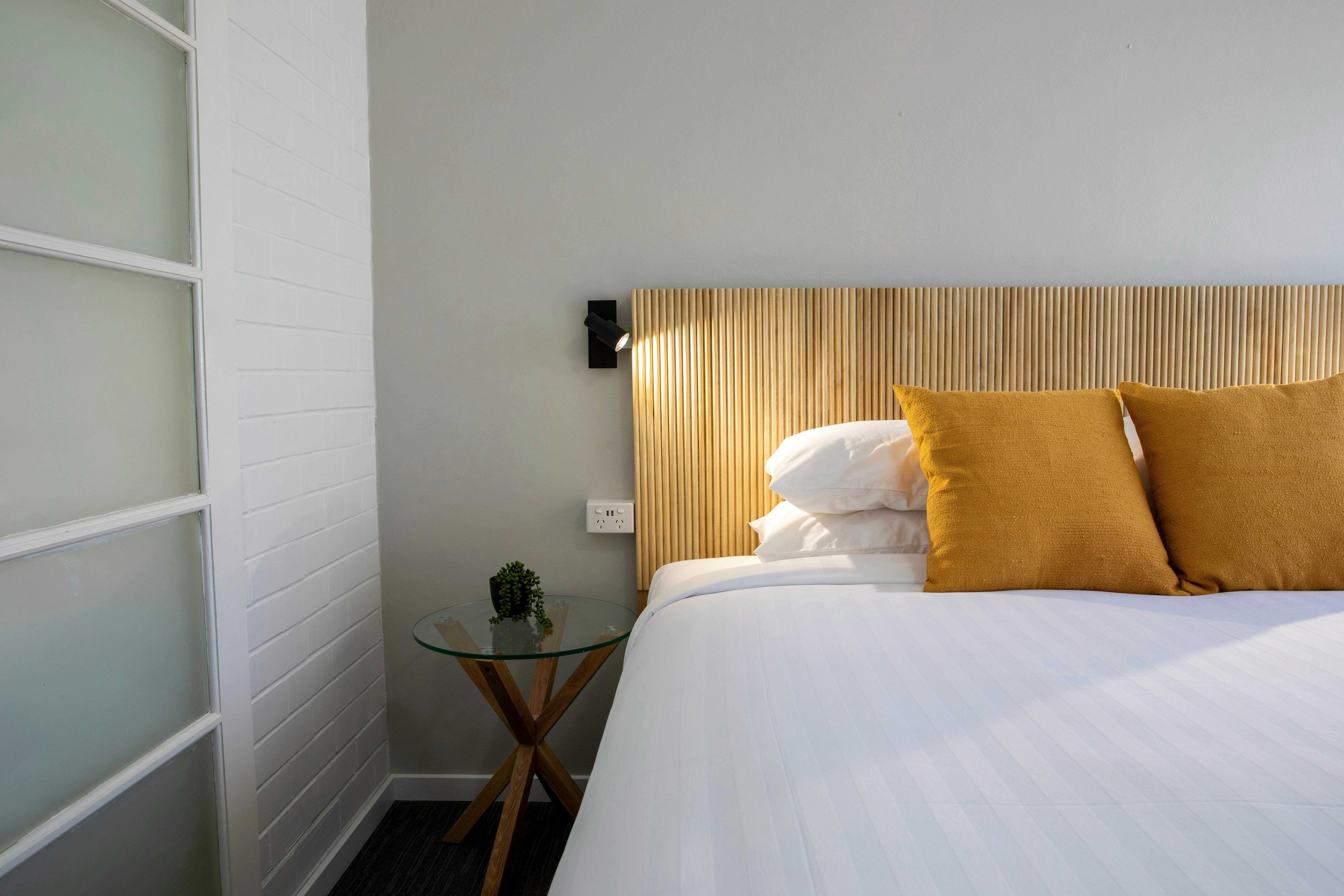 Image of a pillow on a bed in a motel style room with a reading lamp on the wall