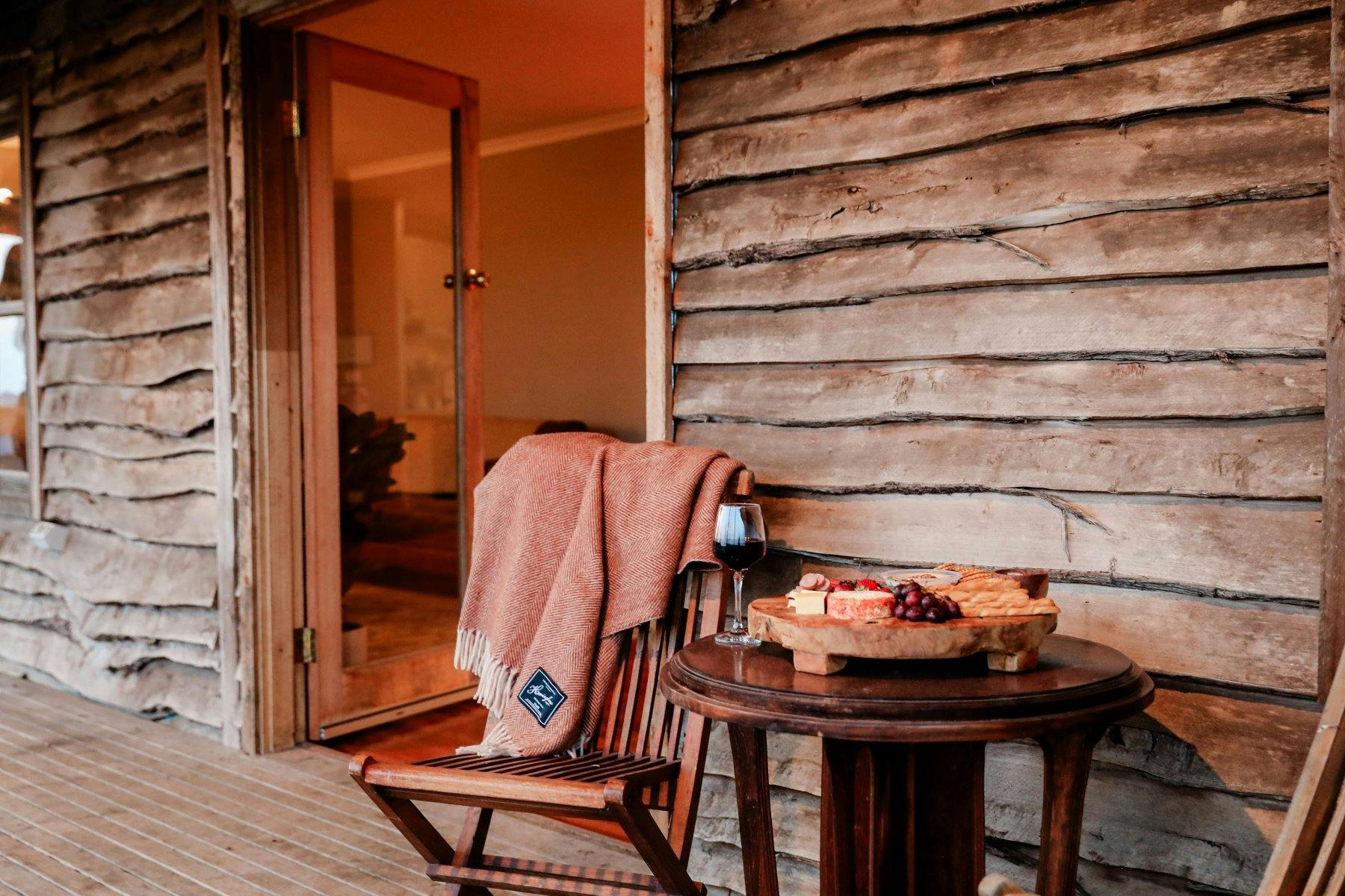 wooden outdoor area with a wooden chair and table with wine and food on it
