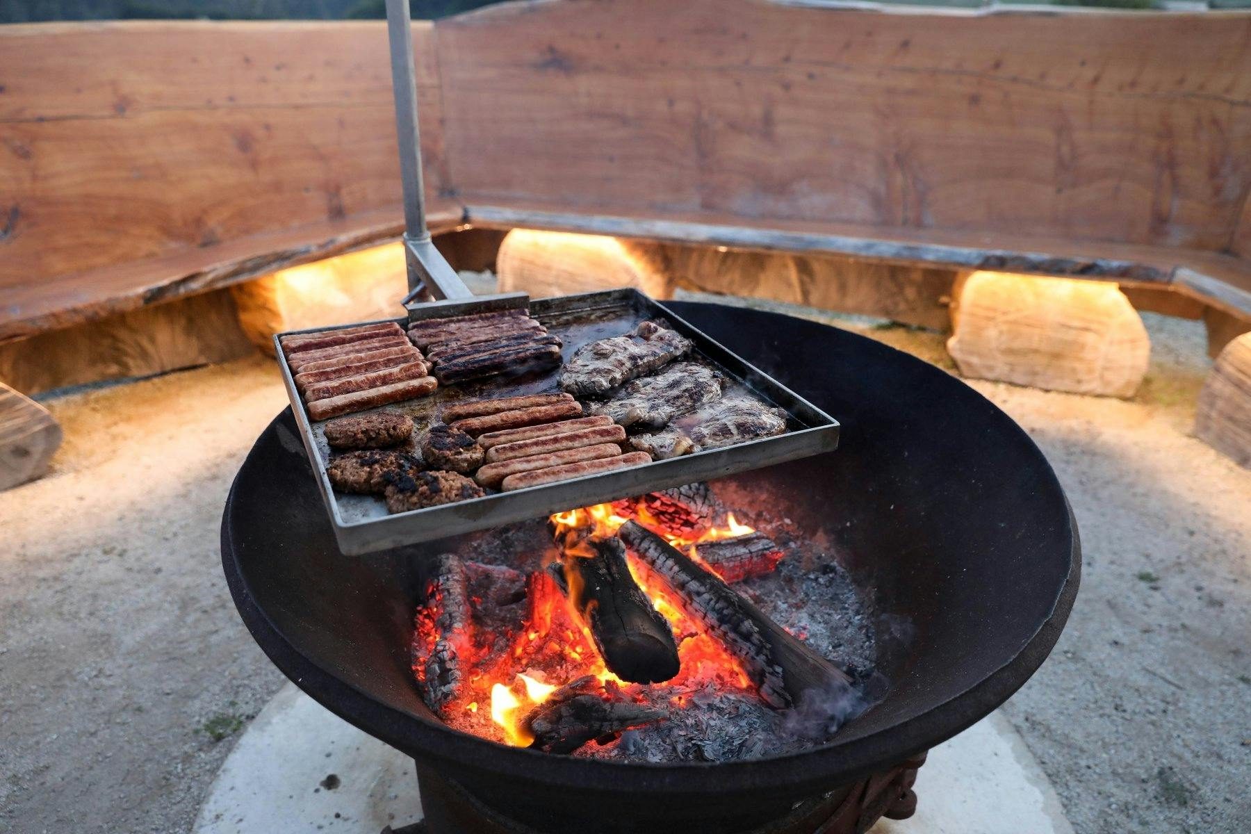 a pan over a charcoal stove with sausages cooking on it