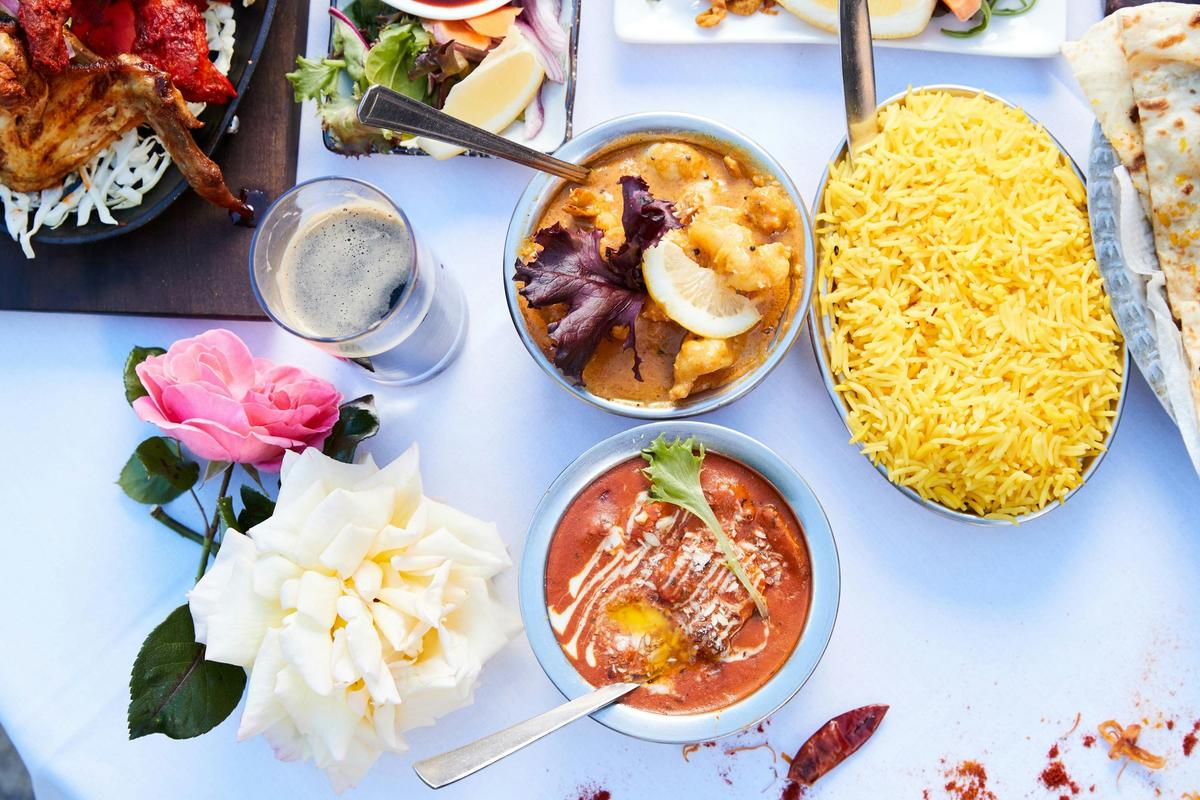 Two bowls of curry and a bowl of rice on a table with flowers next to them.