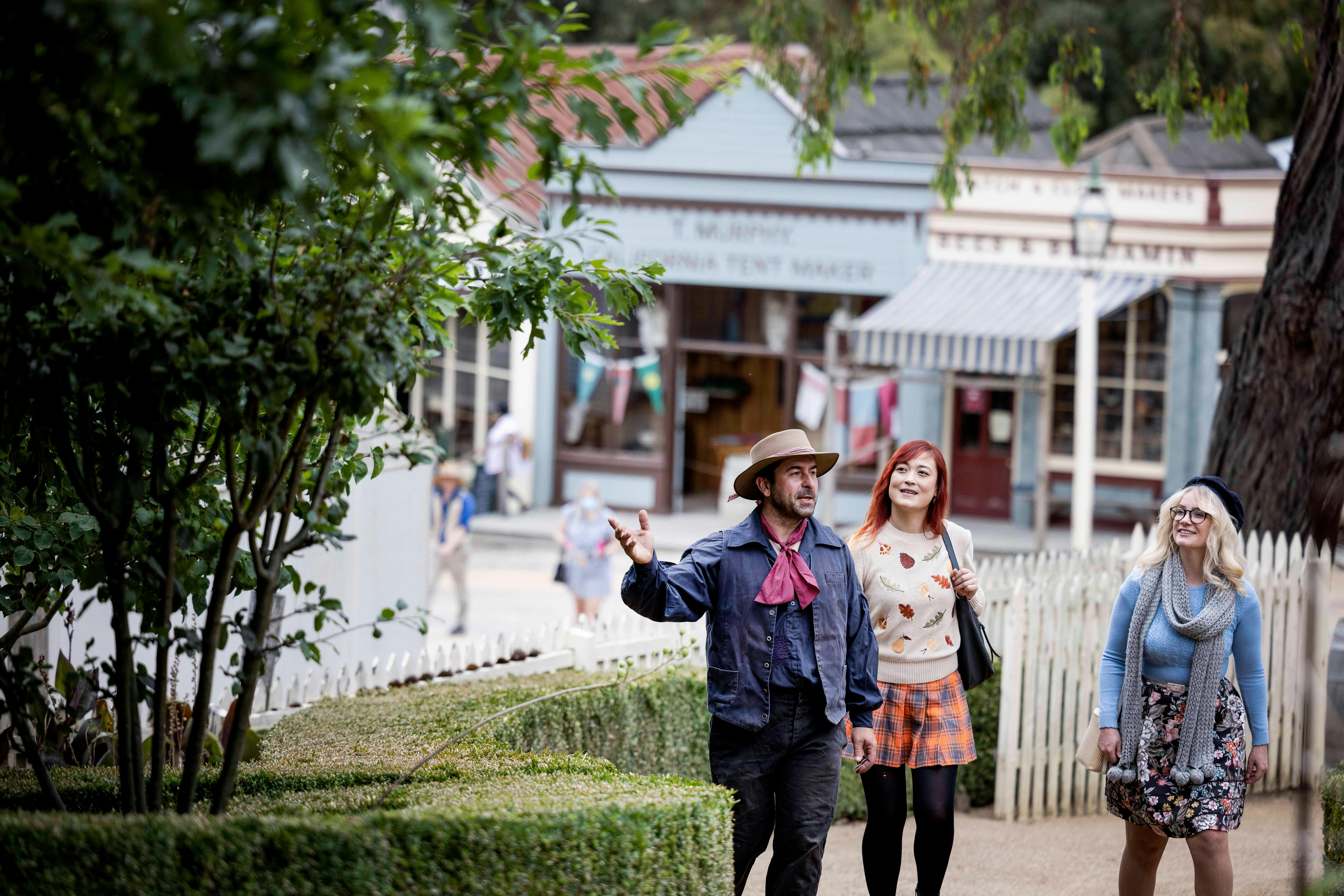 Two women walking through Sovereign Hill gardens with costumed guide
